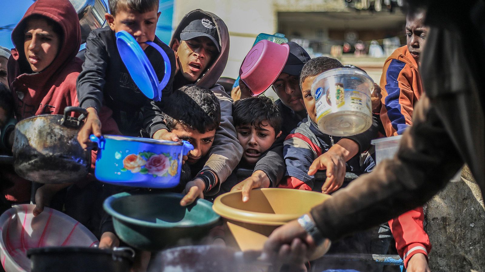 Jóvenes palestinos esperan el reparto de comida con recipientes vacíos en una imagen tomada en Ráfah