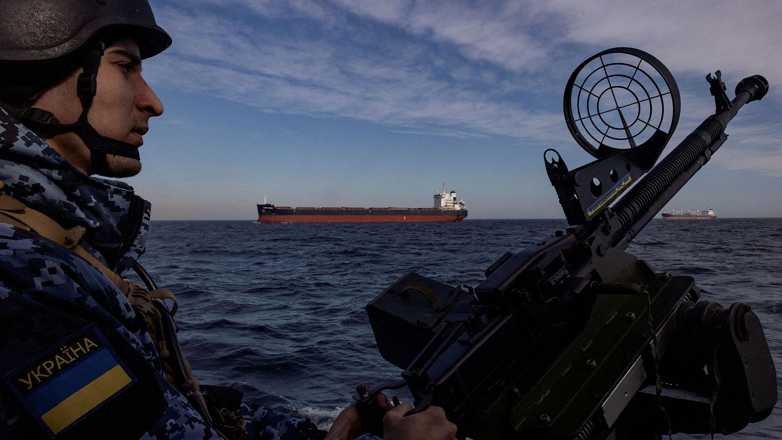 Un militar de la guardia costera de Ucrania maneja un arma en una lancha patrullera mientras un carguero pasa en el Mar Negro
