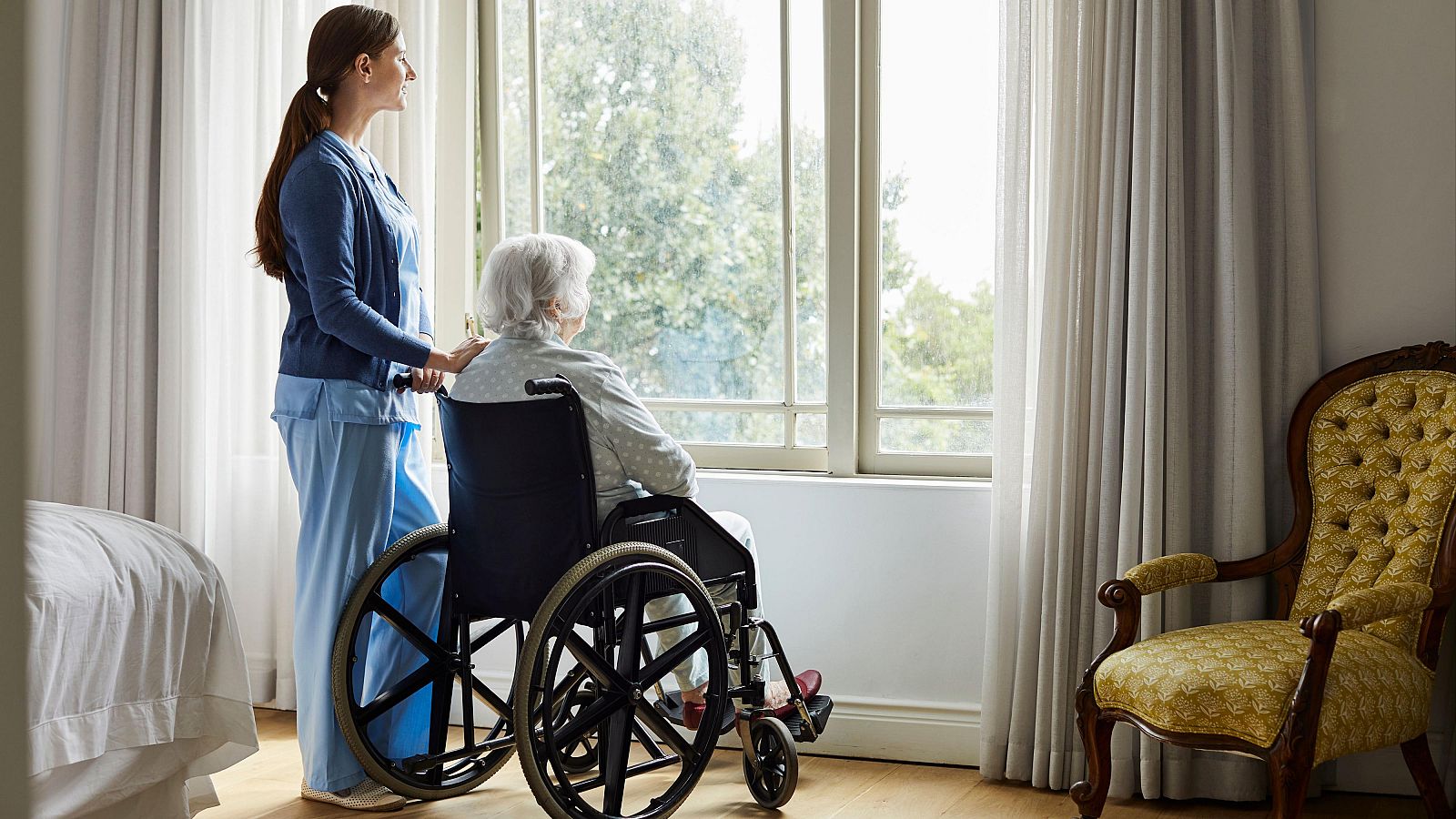 Una mujer en silla de ruedas mira por la ventana en una residencia para mayores