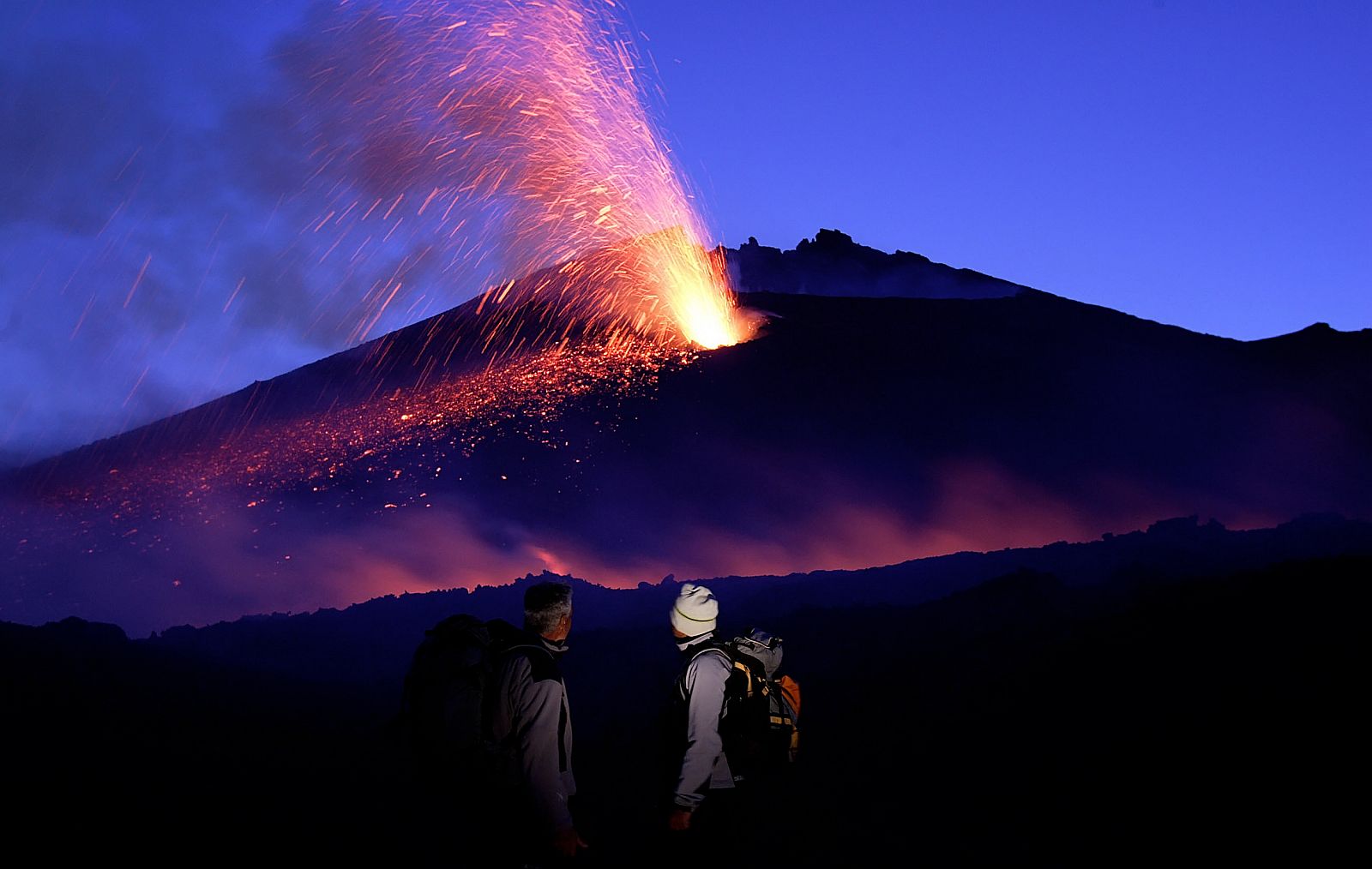 Unos turistas observan el volcán Etna en erupción.