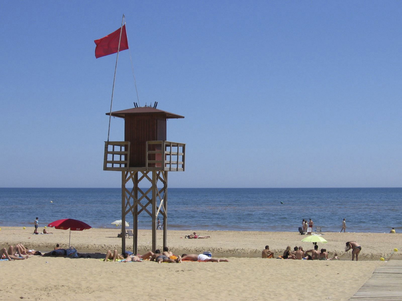 Imagen de la torre de control de Protección Civil de la playa de La Antilla (Huelva), con la bandera roja izada ante la mancha de color rojo descubierta en el agua, lo que ha obligado a cerrar parte de la zona de baño.