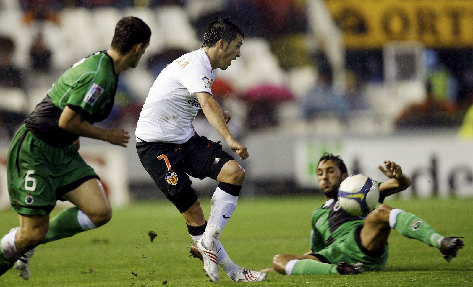 El delantero del Valencia David Villa remata a portería ante la presión de los jugadores del Racing.