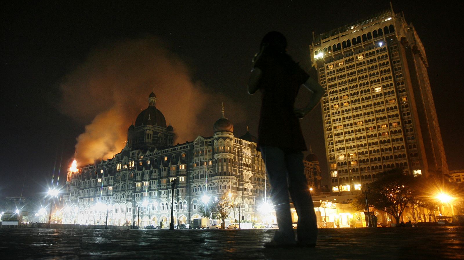 A reporter talks on phone as smoke is seen coming from  Taj Hotel in Mumbai