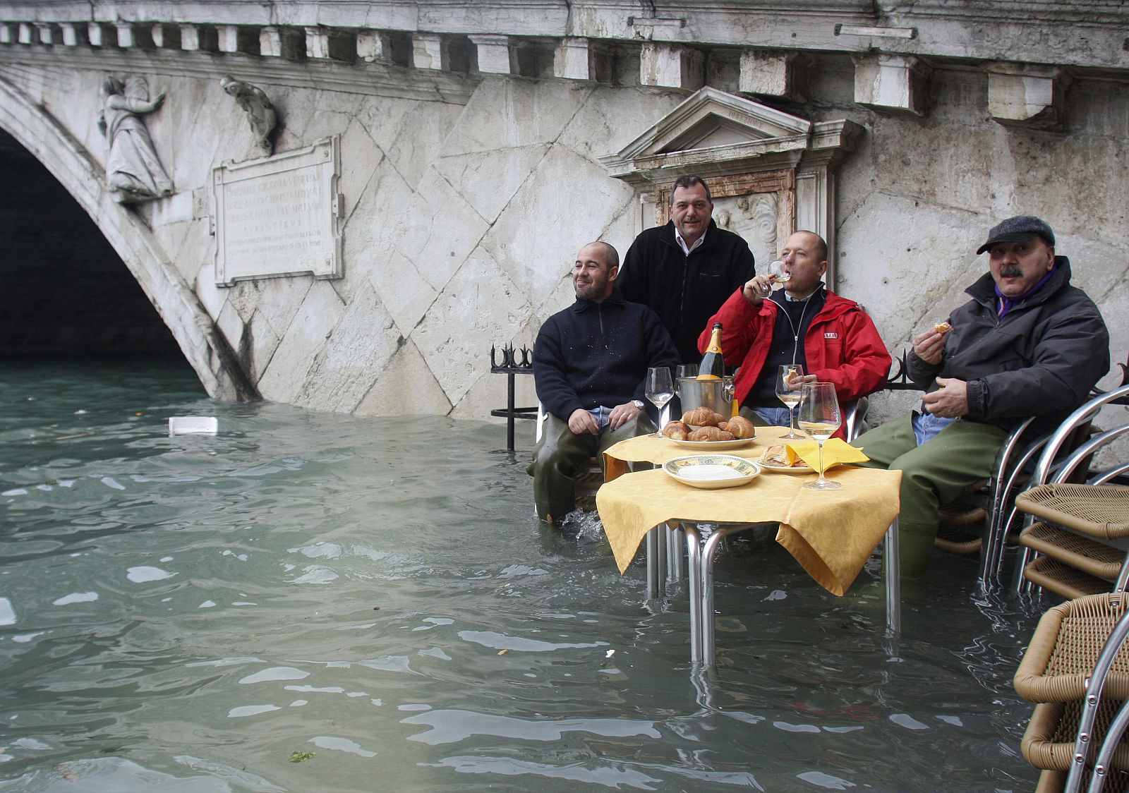 Un grupo de gondoleros desayuna en Venecia a los pies de un puente inundado.
