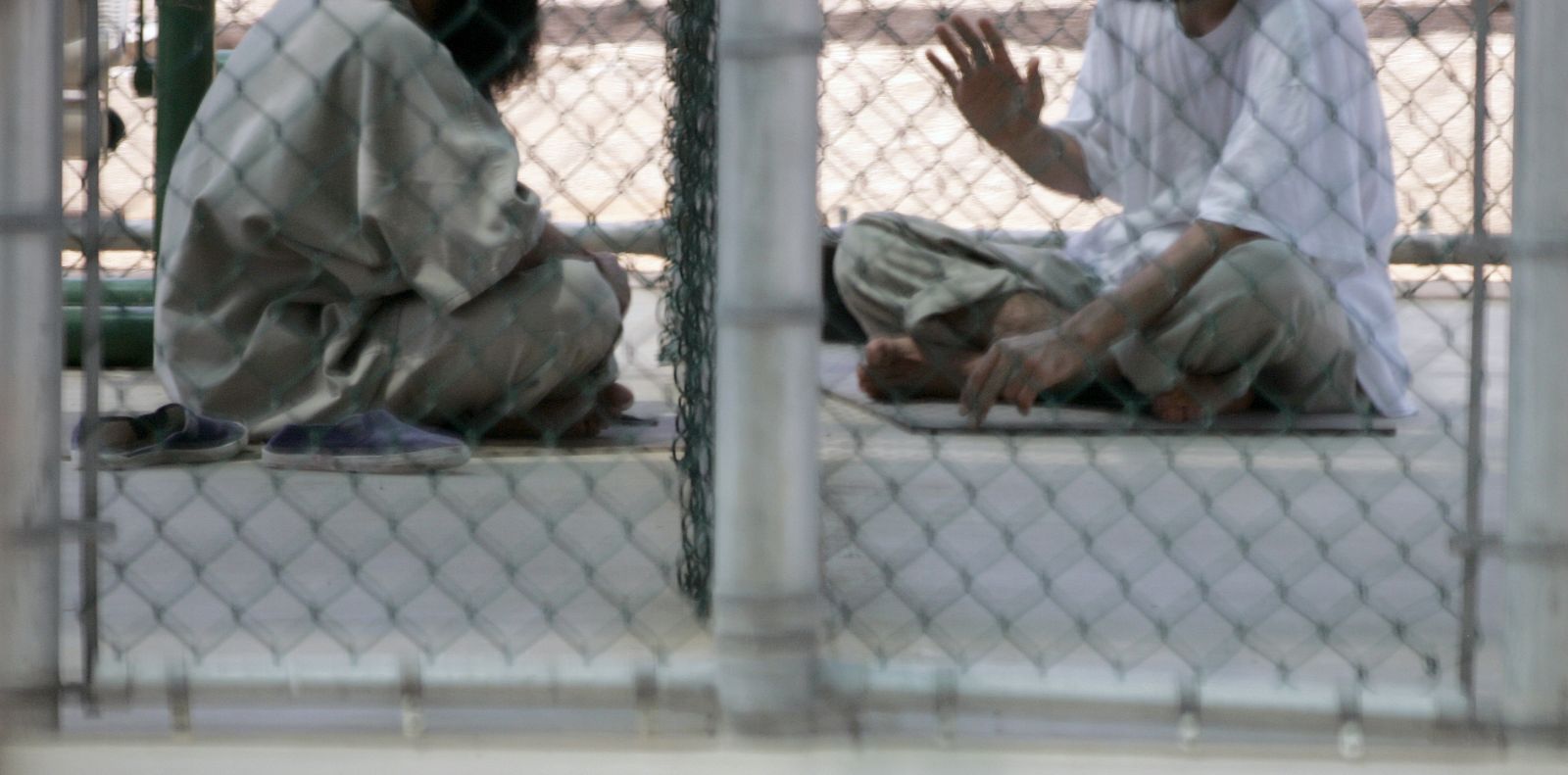 Dos hombres detenidos en el Campo VI de la prisión de Guantánamo en septiembre de 2007 conversan sentados en el suelo.