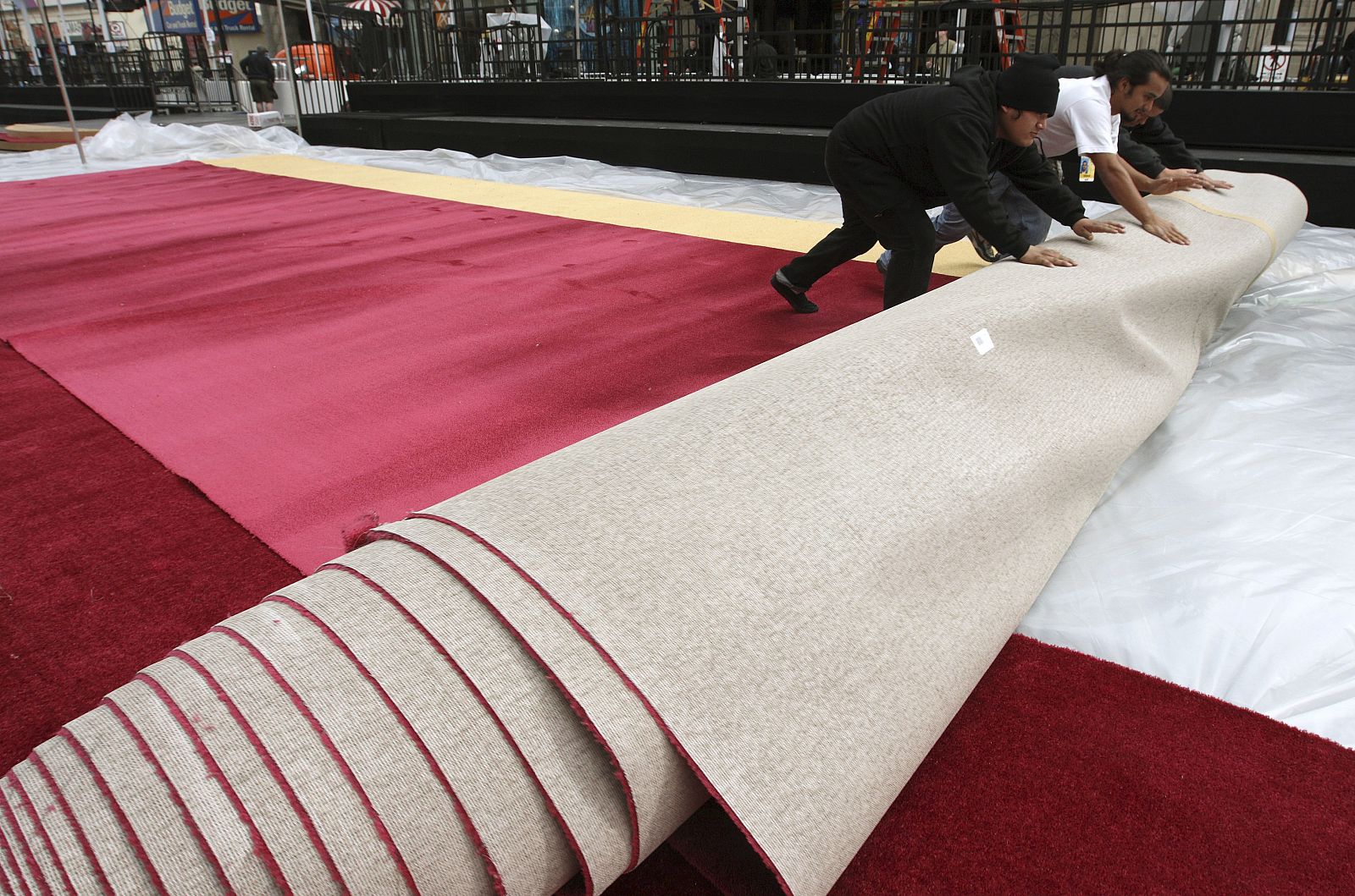 Unos trabajadores desenrollan la alfombra roja sobre la que luego pisarán las estrellas.