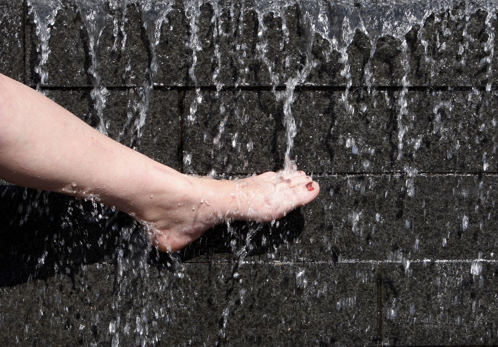 Una mujer se refresca el pie en una fuente