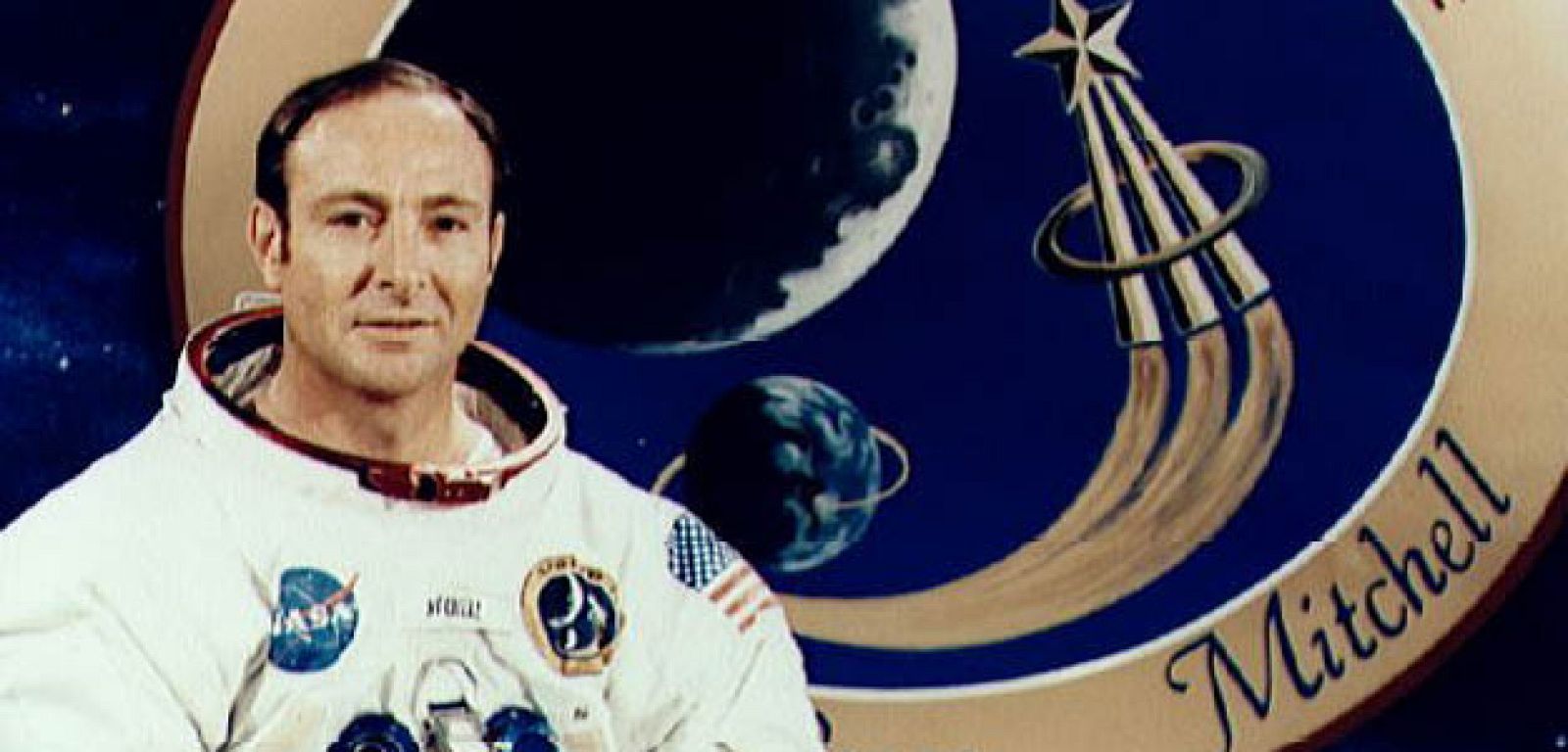Edgar Mitchell, piloto del Apolo 14 delante de la insignia de la misión.
