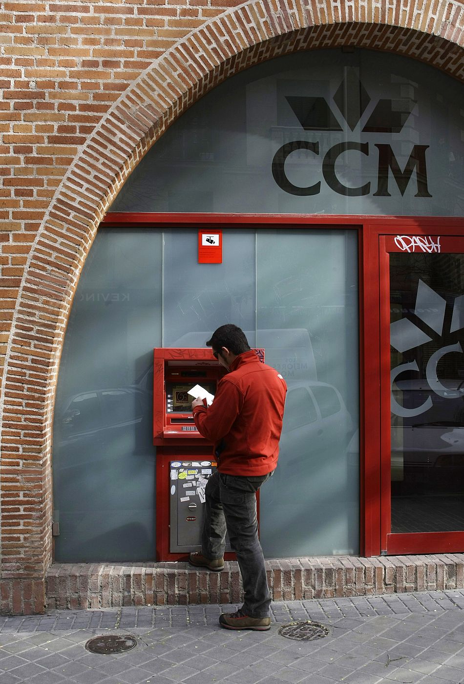 A man uses an ATM machine outside a branch of savings bank Caja Castilla La Mancha in central Madrid