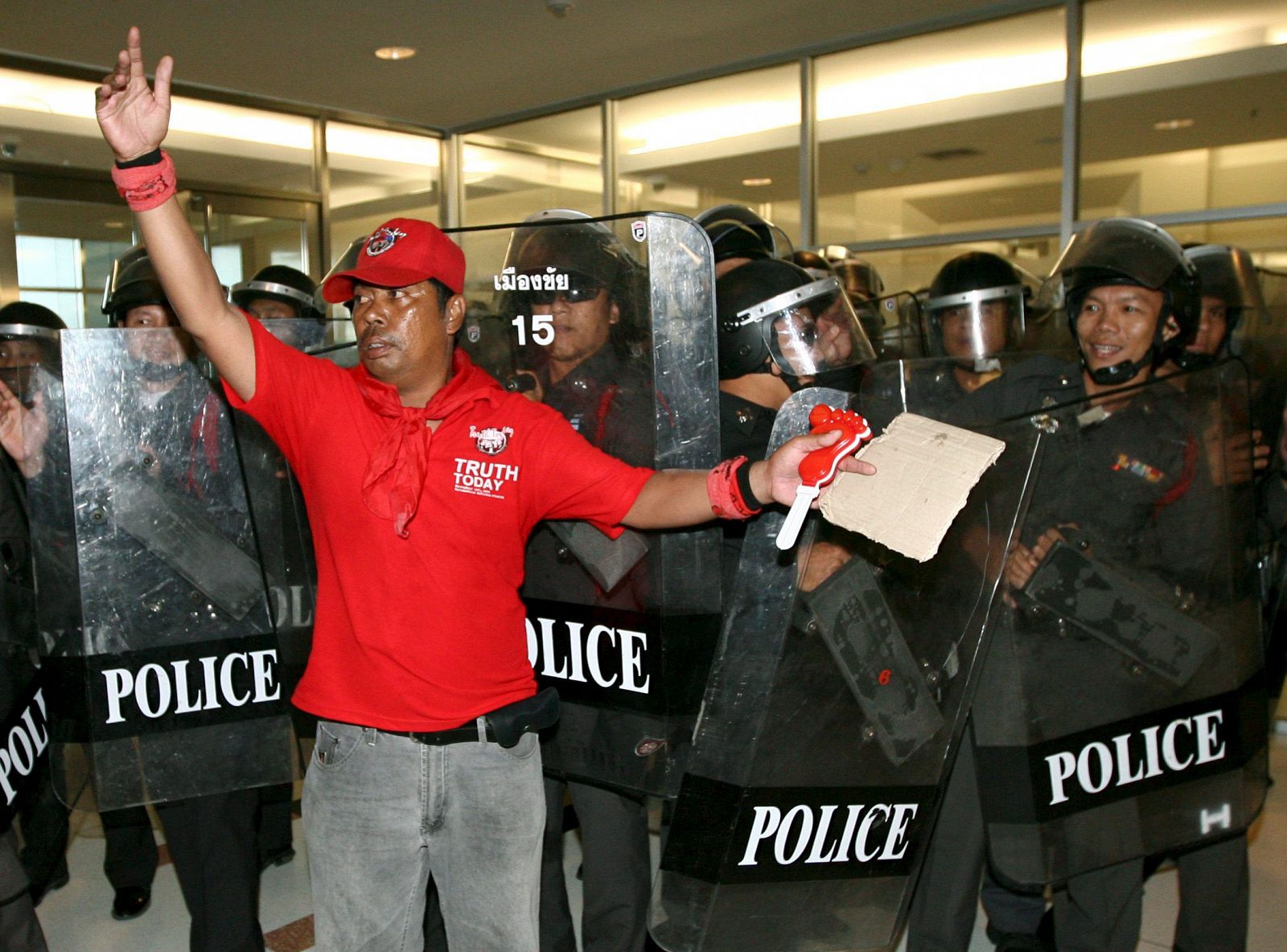 Un manifestante de los "camisas rojas" se coloca ante una barrera de policias antidisturbios tras irrumpir en la Comisión Electoral de Tailandia