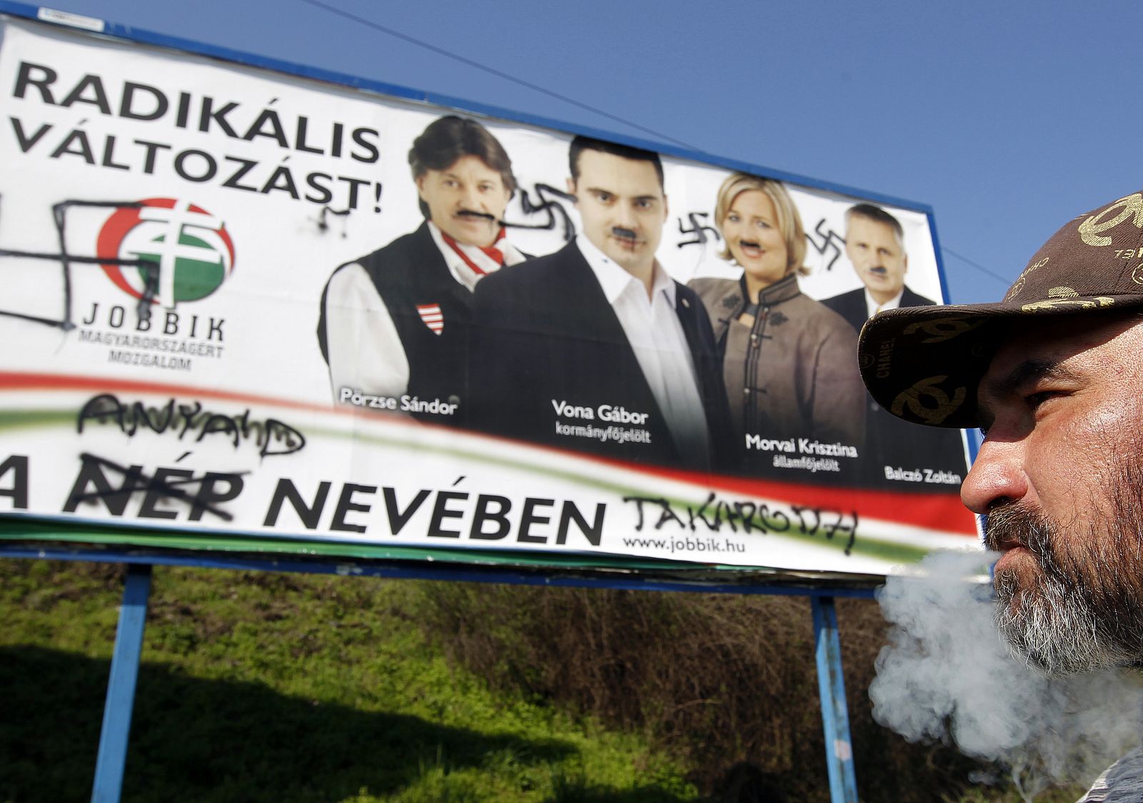 Un vagabundo fuma frente a un cartel del partido Jobbik pintado con símbolos nazis.