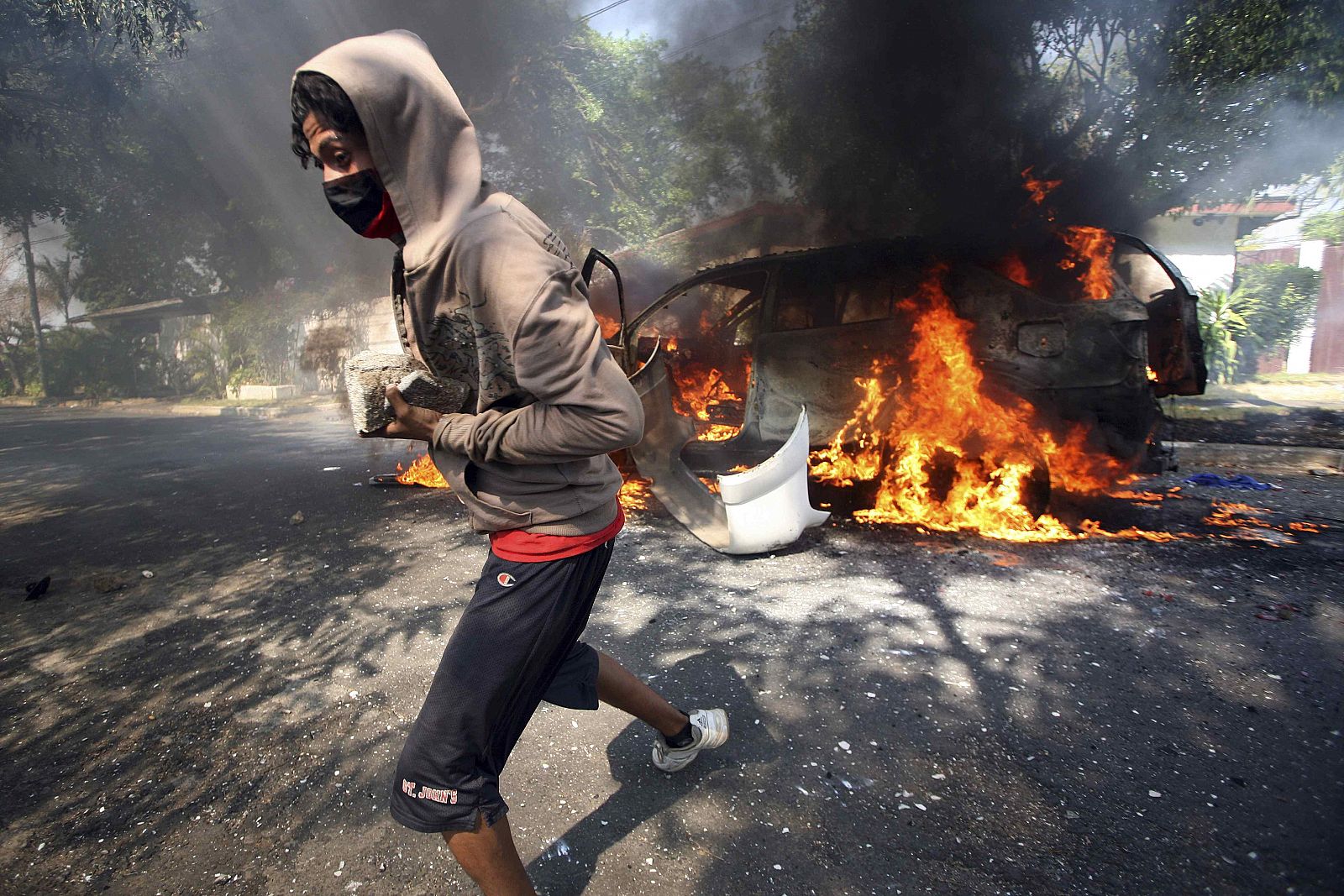Un sandinista pasa junto a un coche en llamas cargado con piedras