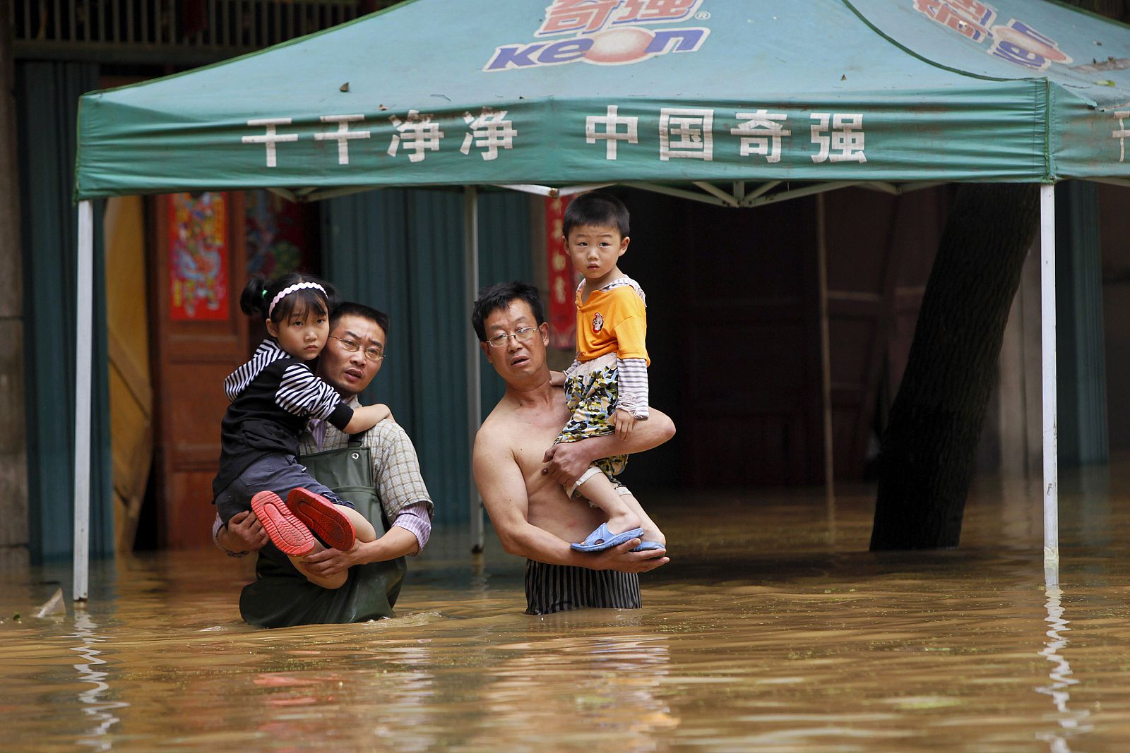 Unos padres, víctimas de las lluvias torrenciales, llevan a sus hijos en brazos por una calle inundada a la espera de que un bote los rescate en Fuzhou.