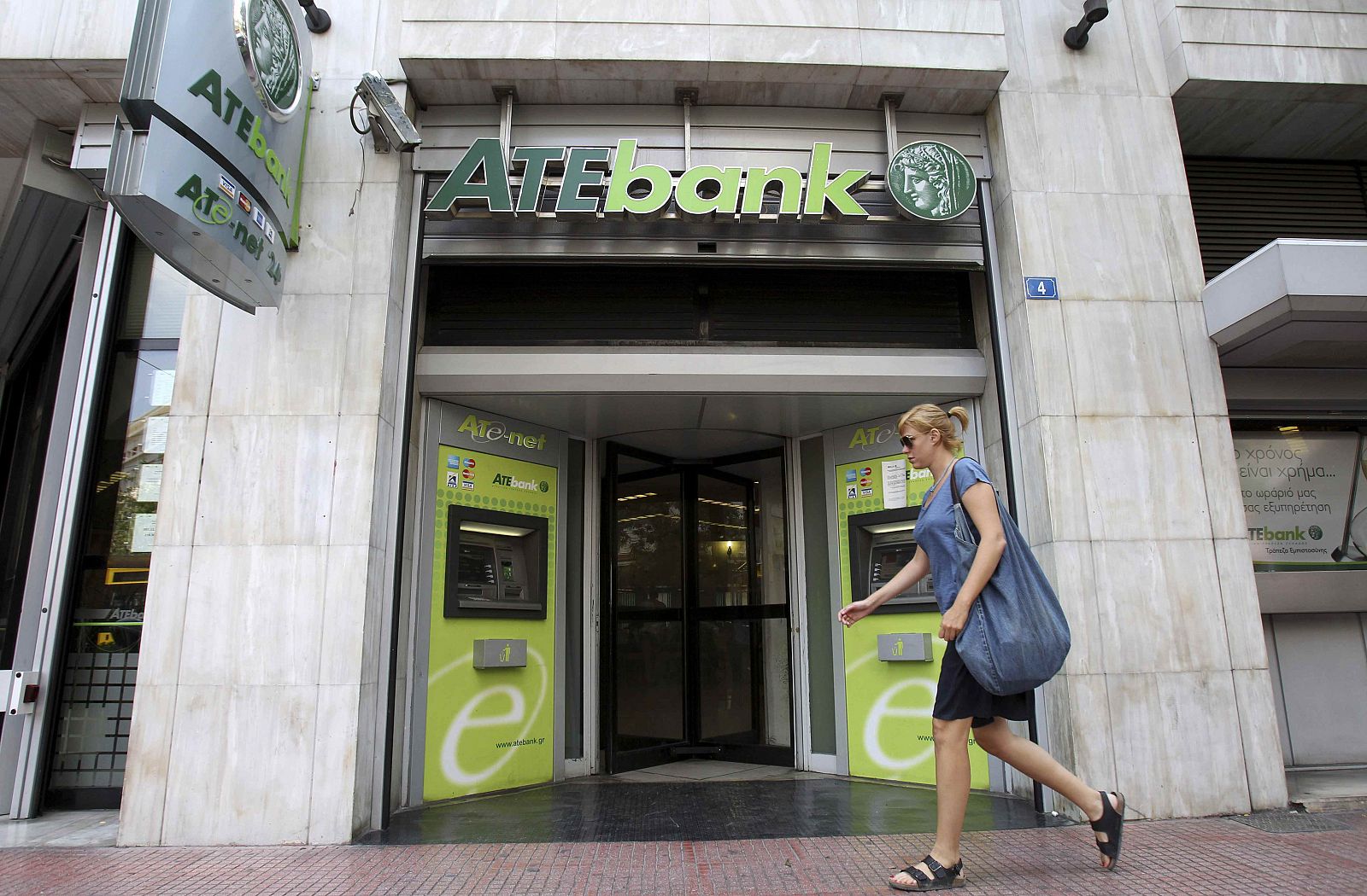 A woman walks in front of a branch of ATEbank in Athens