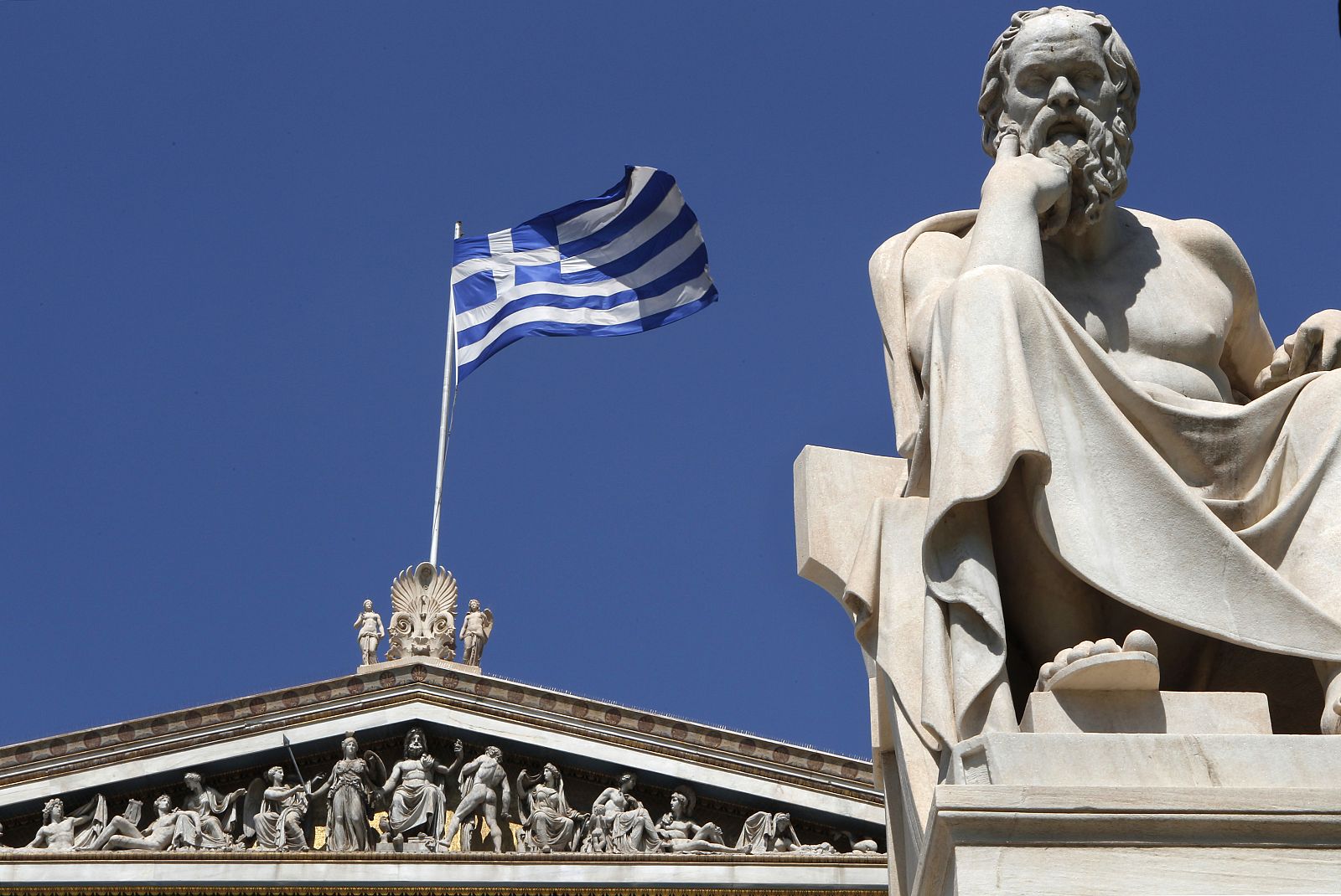 Una bandera griega ondea detrás de la estatua de Sócrates en Atenas
