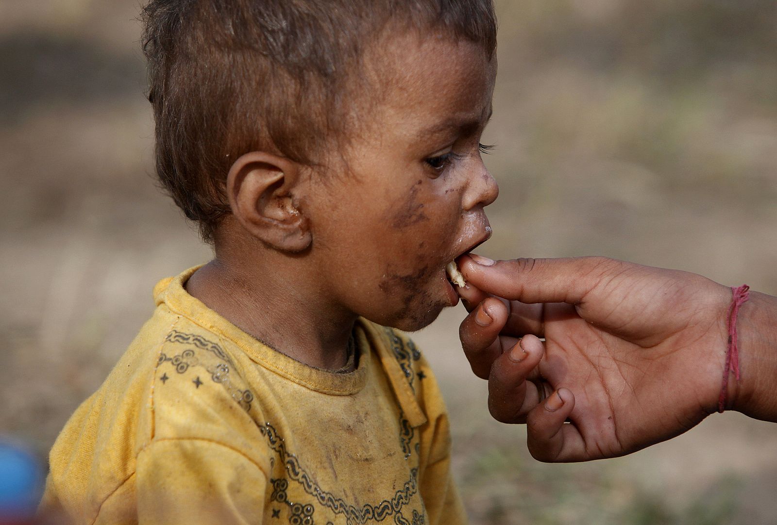 Un niño de dos años, alimentado por su hermana en un campamento de Pakistán.