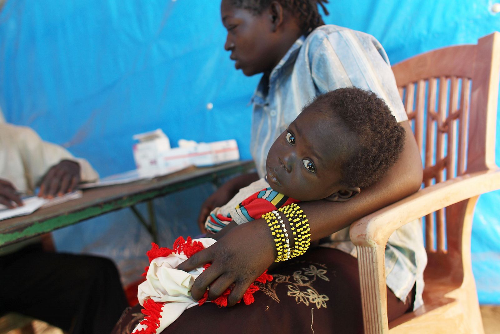 Una mujer congolesa sostiene en brazos a su hija enferma de malaria mientras habla con un doctor de Médicos Sin Fronteras.