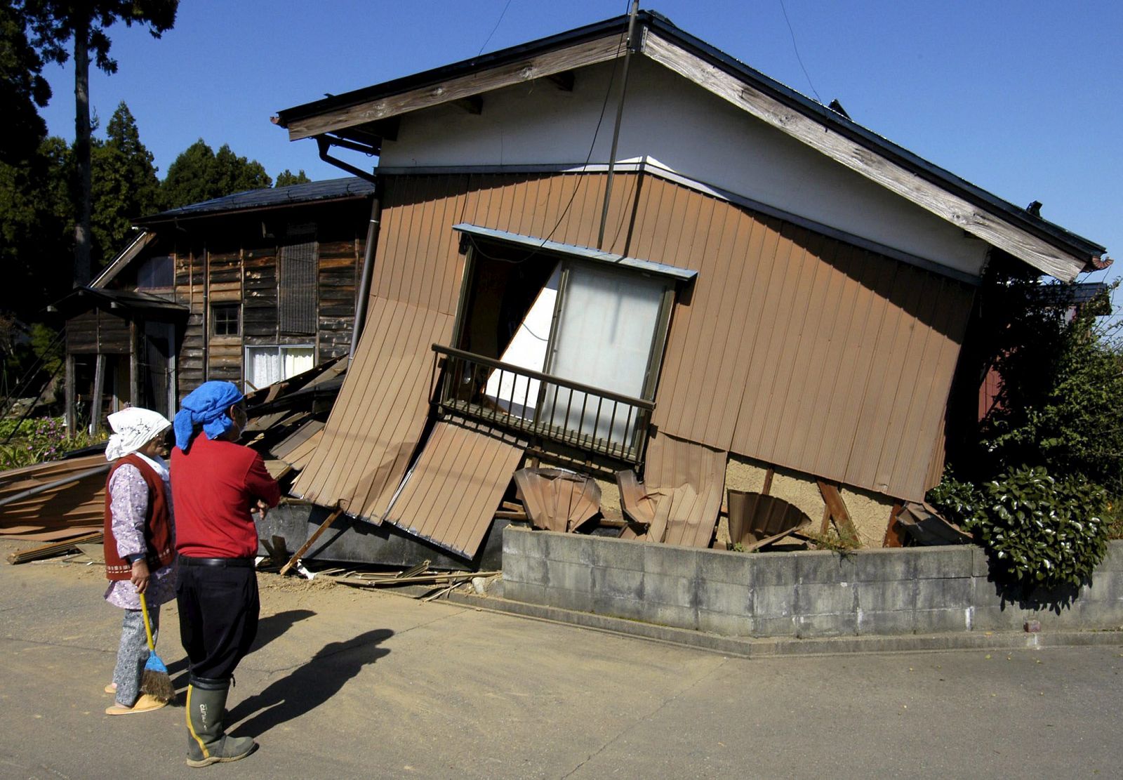 Fotografía de archivo tomada el 24 de octubre de 2004 que muestra a una mujer y su vecino observando su casa derruida tras un terremoto de 6,8 grados de magnitud el día anterior en Ojiya al noroeste de Tokio en Japón