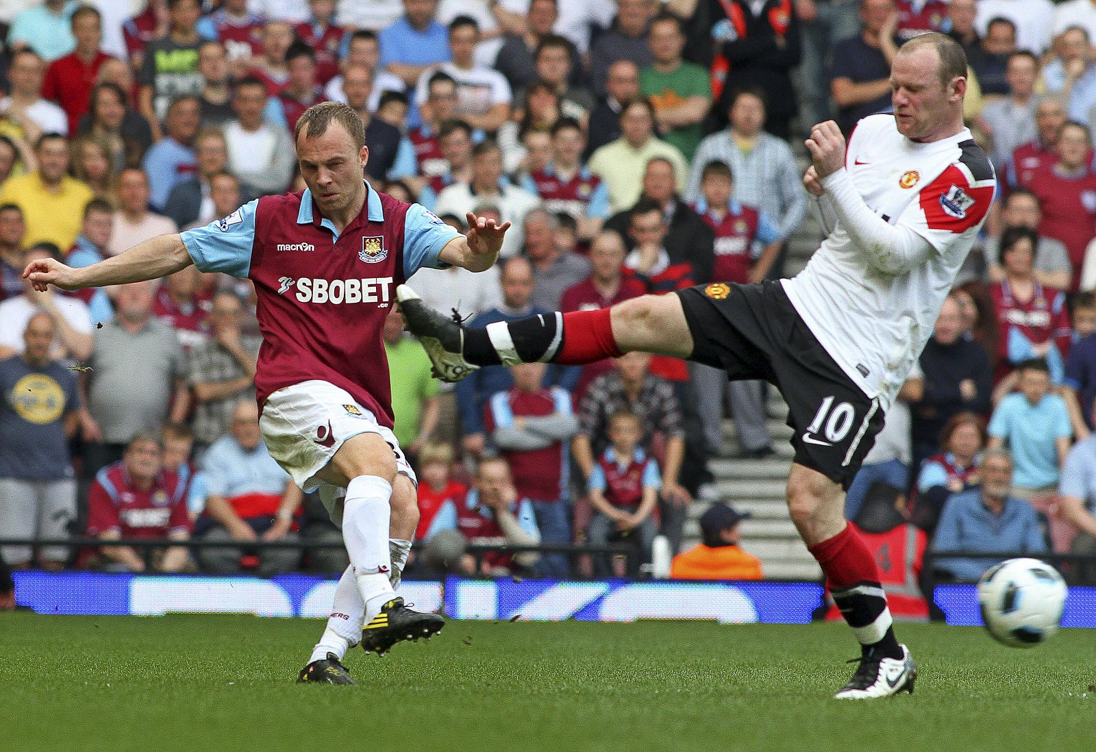 Wayne Rooney (d) trata de impedir el disparo de Lars Jacobsen (i), del West Ham