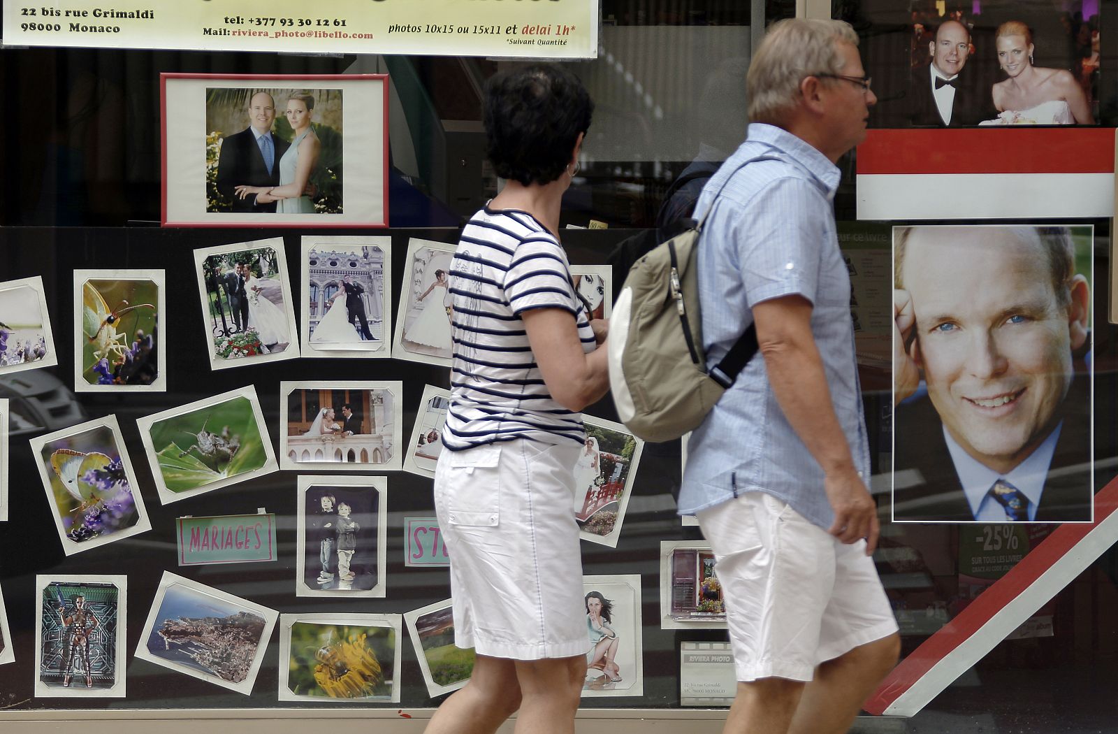 Turistas pasan por un escaparate de Mónaco con fotos de la pareja real.