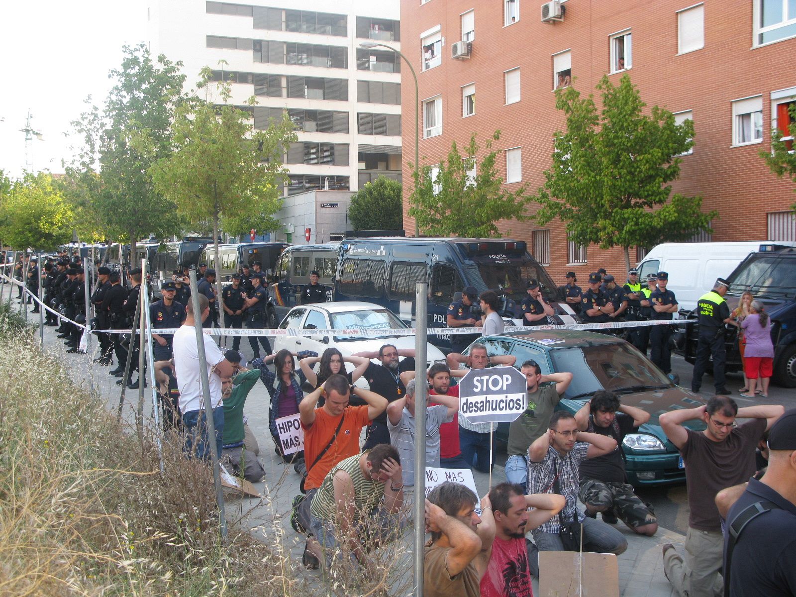 Varios manifestantes se arrodillan junto a un cordón policial en Carabanchel en señal de protesta por el desahucio de una mujer y su hijo de 16 años.