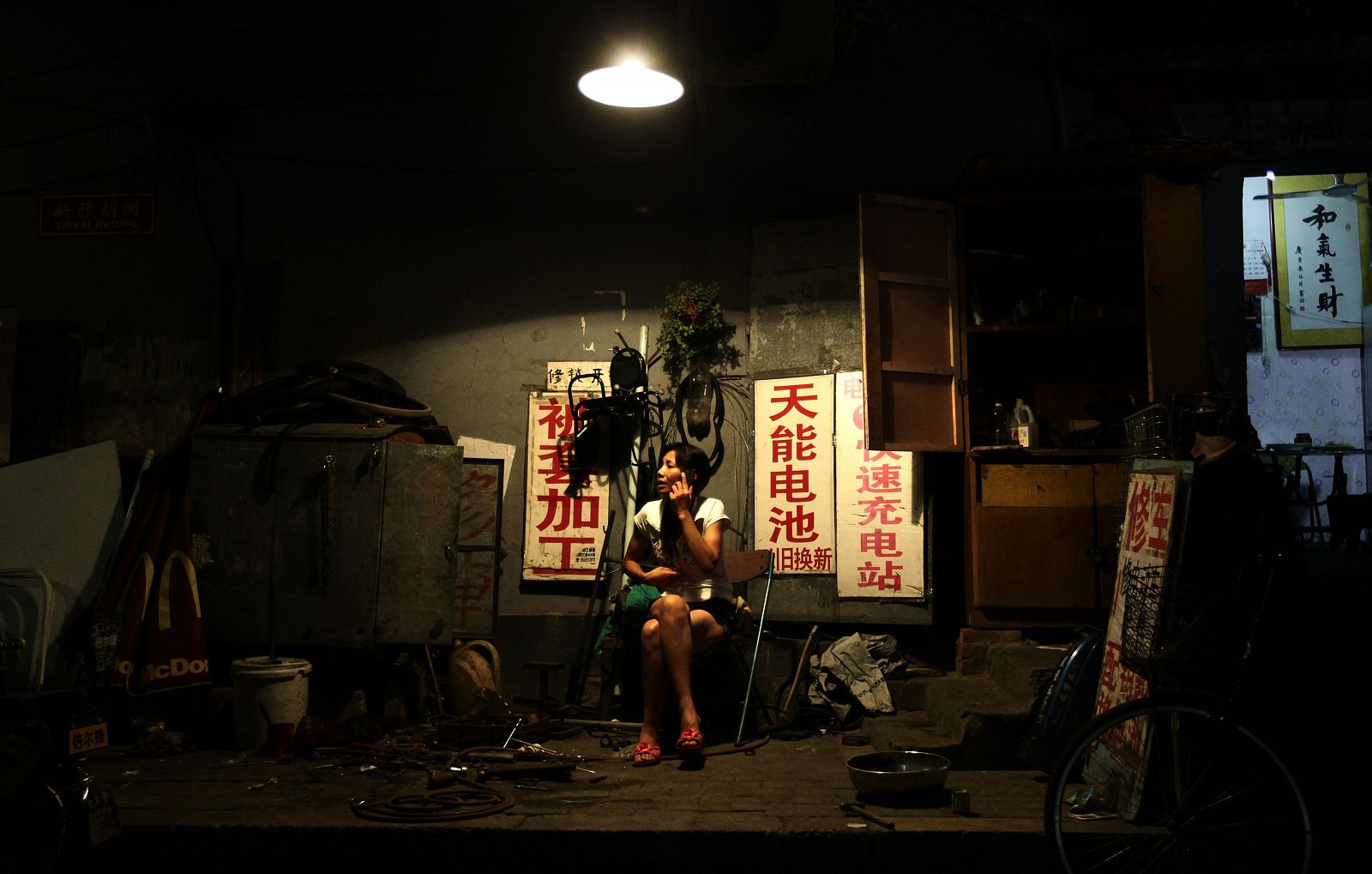 Una mujer usa el móvil en la entrada de una tienda de reparación de bicicletas en Beijin