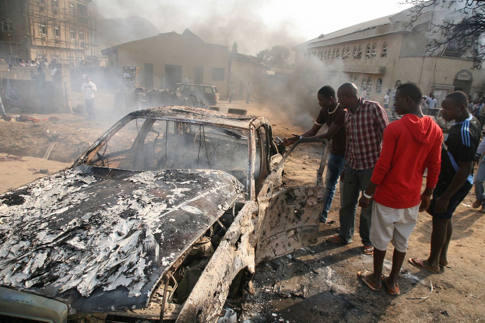 Unos hombres observan un coche quemado después de un ataque a cristianos en Nigeria.