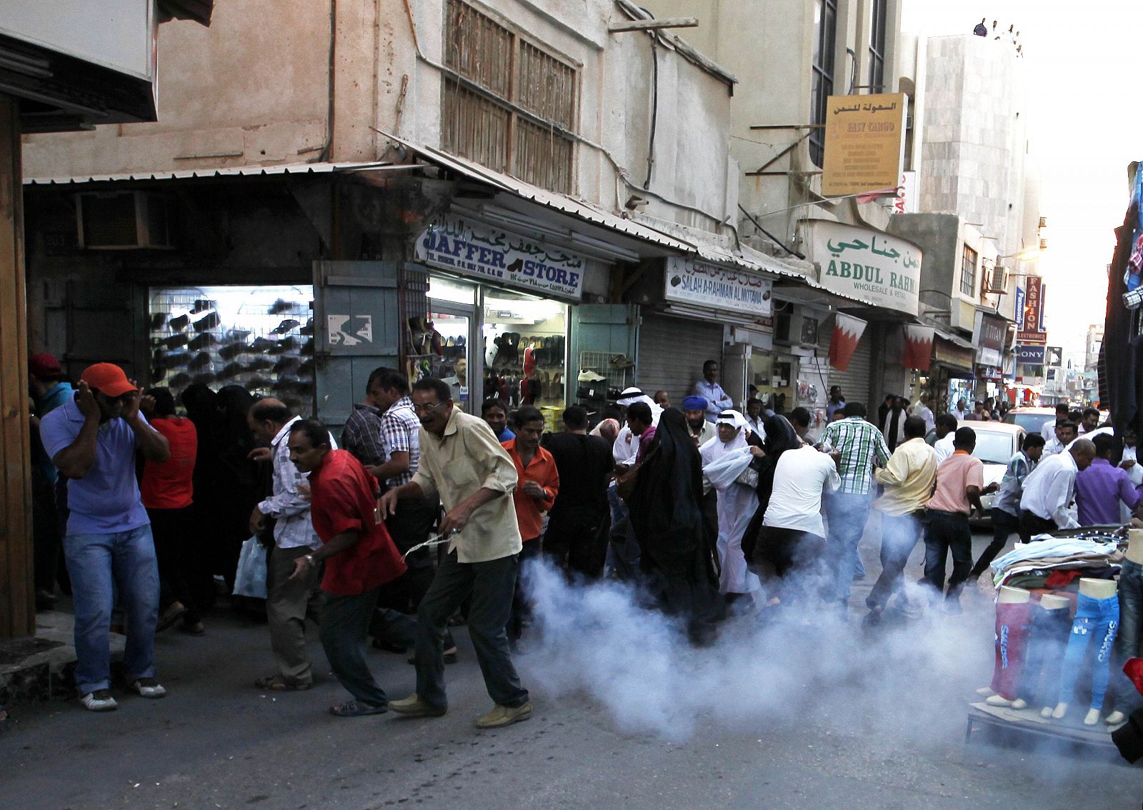 Manifestantes y comerciantes se protegen de una granada de sonido durante una protesta en la capital de Baréin, Manama, el 26 de octubre