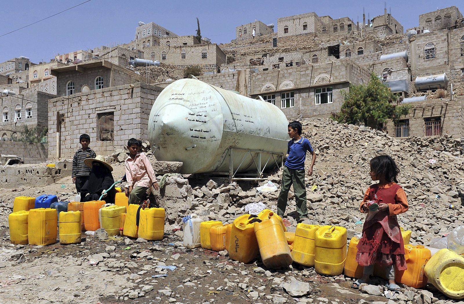 Una mujer y unos niños llenan bidones de agua de una tubería pública en una barriada pobre de Saná (Yemen).