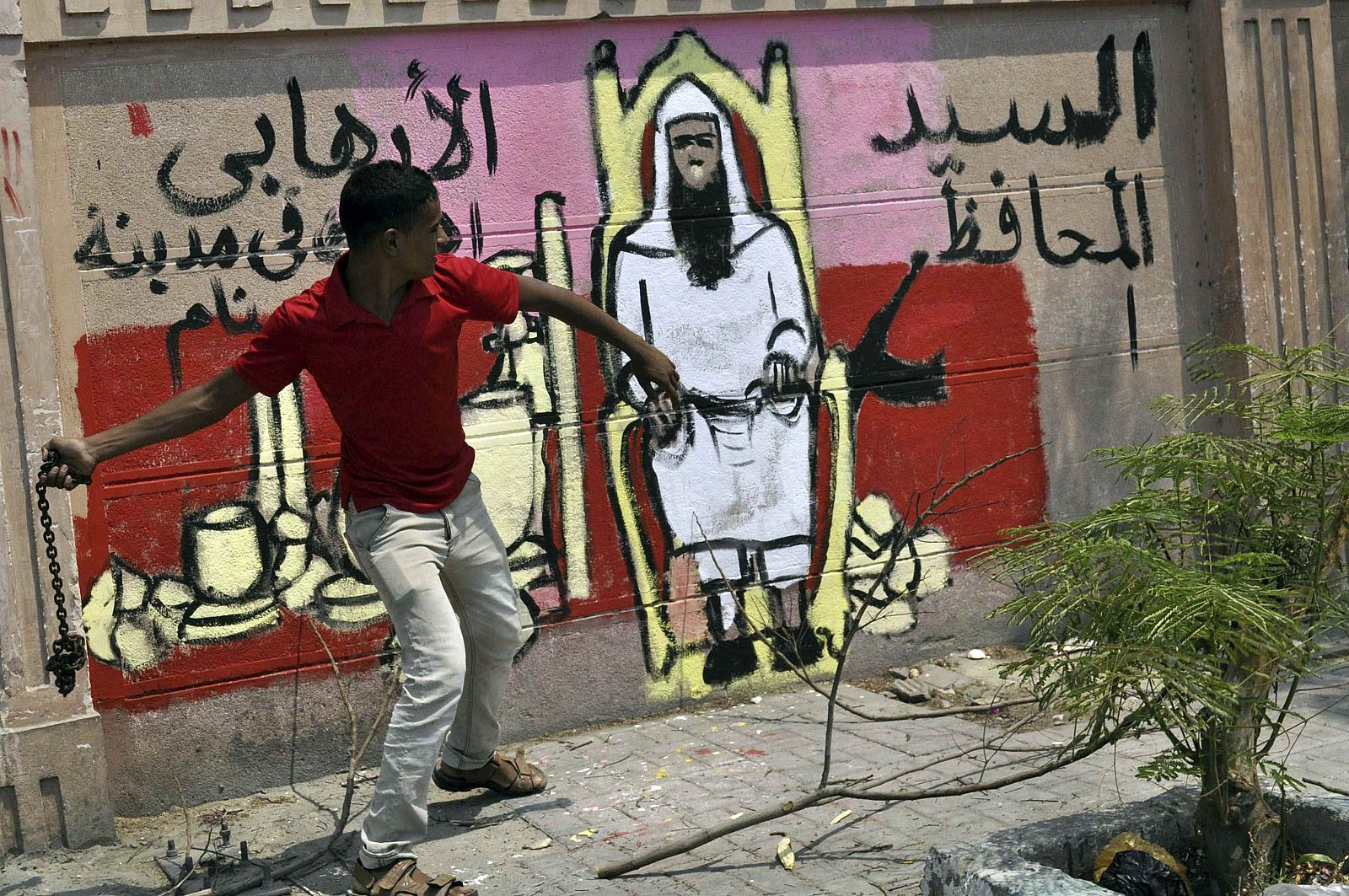 Un manifestante lanza una cadena junto a un grafiti que caricaturiza al islamista designado como gobernador de Luxor.