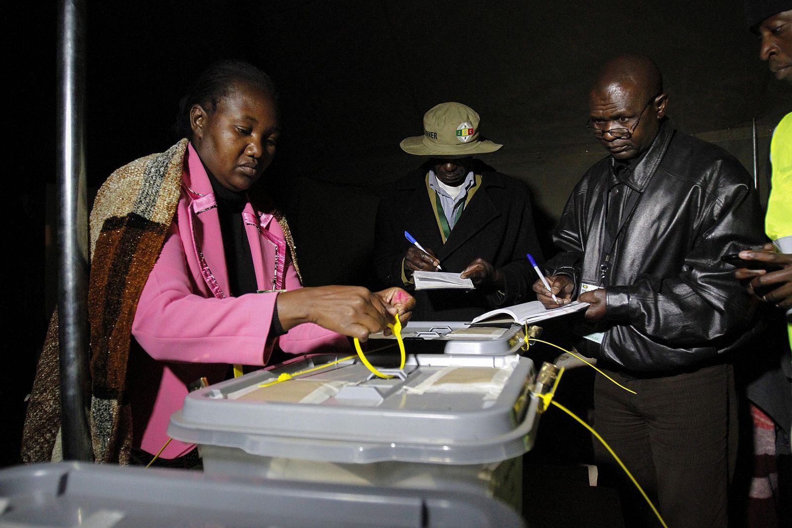 Miembros de la Comisión Electoral de Zimbabue observan mientras se sellan las cajas de votación tras el cierre de los colegios electorales