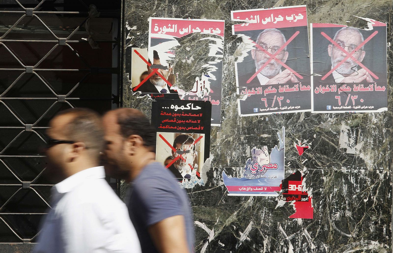 Dos ciudadanos caminan tras un cartel de Morsi