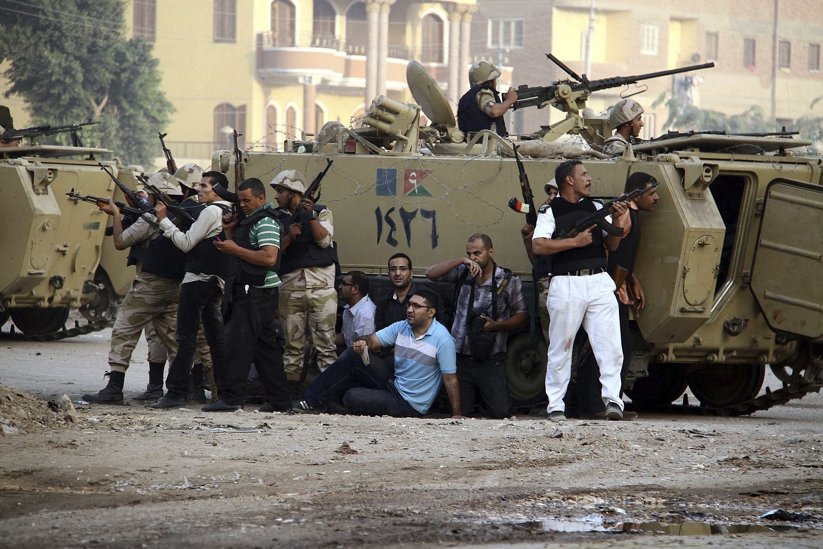 Soldados egipcios y periodistas locales se cubren tras un vehículo armado durante una operación contra un grupo de hombres armados en un suburbio de El Cairo, Egipto