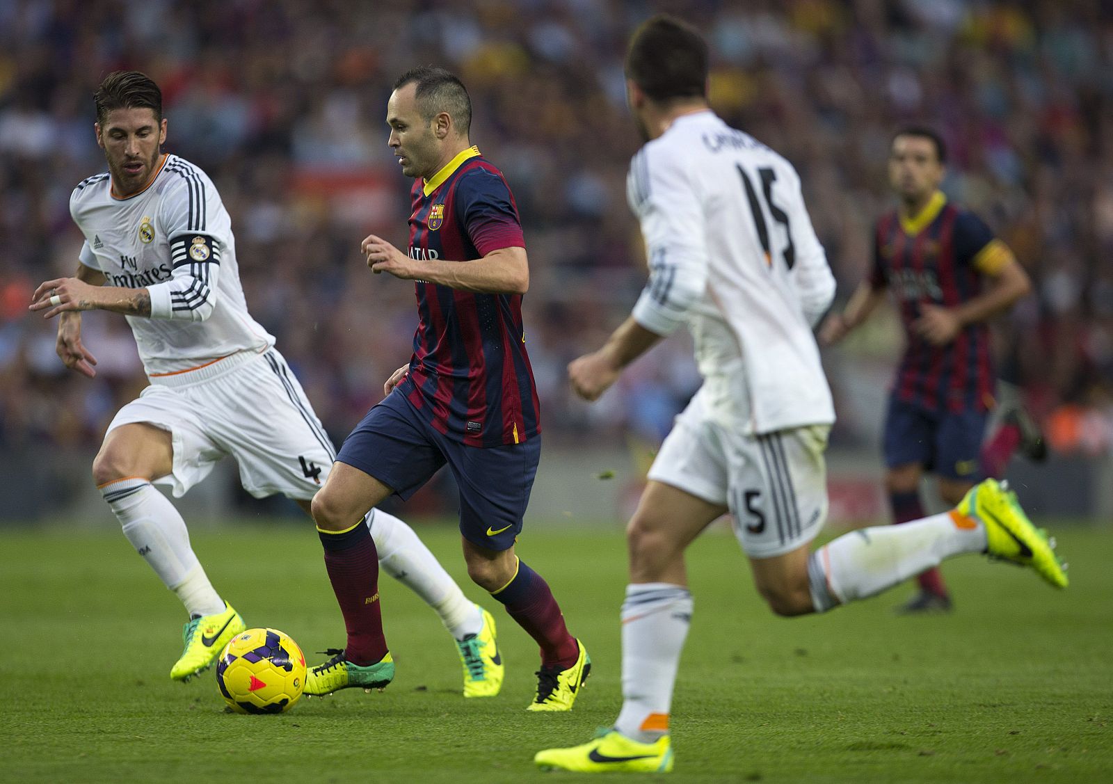 El centrocampista del F.C. Barcelona Andrés Iniesta, con el balón ante el defensa del Real Madrid Sergio Ramos.