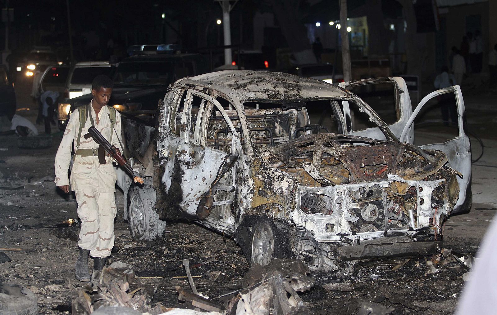 Somali policeman walks past a burnt car after an explosion outside the Maka Al-Mukarama hotel in Somalia's capital Mogadishu