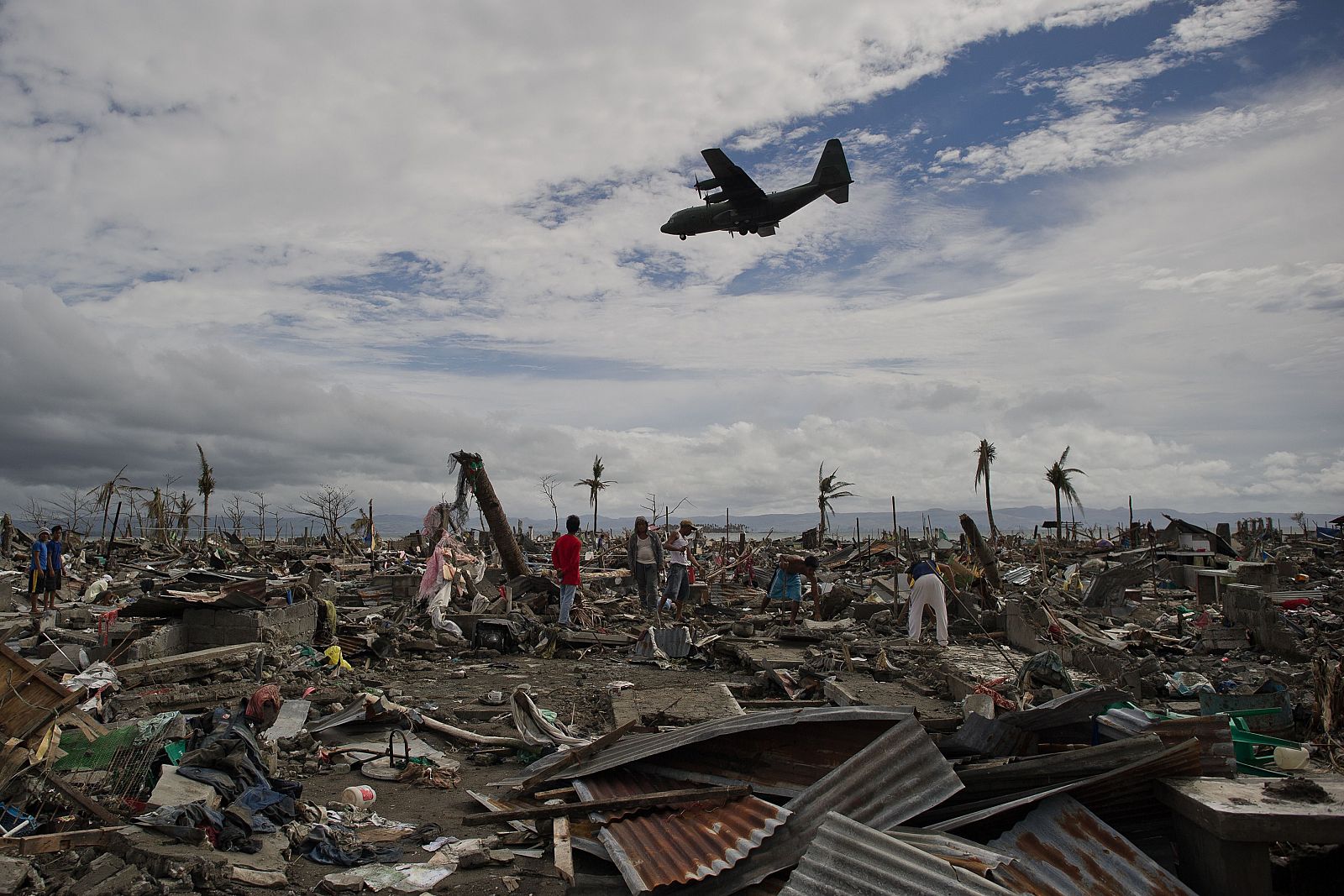 Damnificados del tifón Haiyan, entre las ruinas de sus casas mientras un avión con ayuda se dirige al aeropuerto de Tacloban