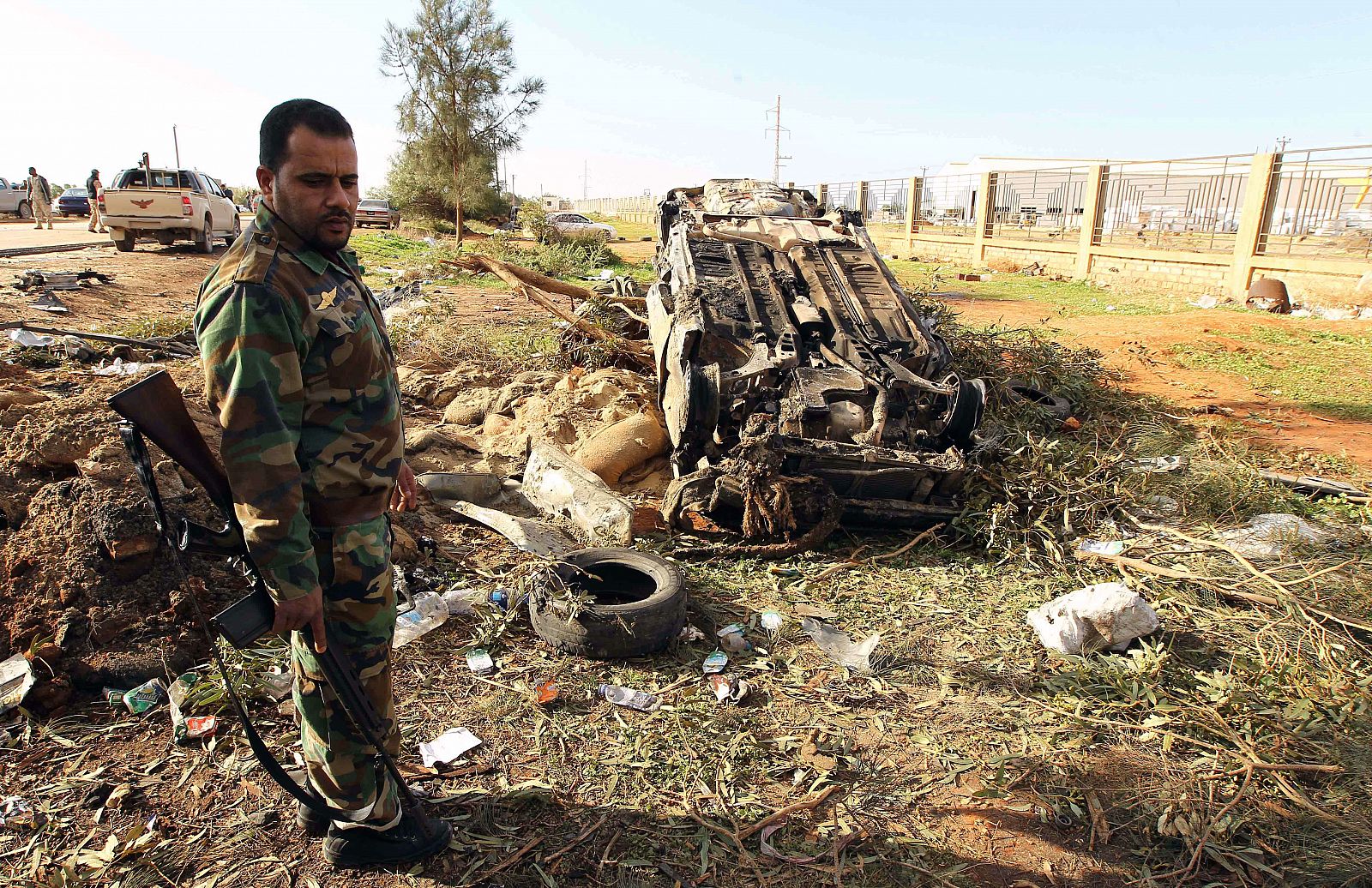 Un miembro de las fuerzas de seguridad de Libia, junto a uno de los vehiculos destruidos en el ataque con coche-bomba en Bengasi