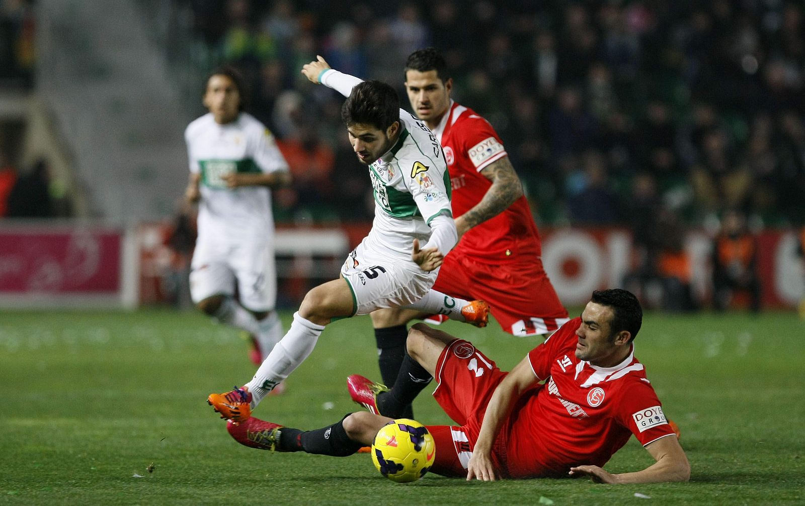 El jugador del Elche Carlos Gil (i) trata de superar la entrada de Iborra (d), del Sevilla, durante el partido de Liga