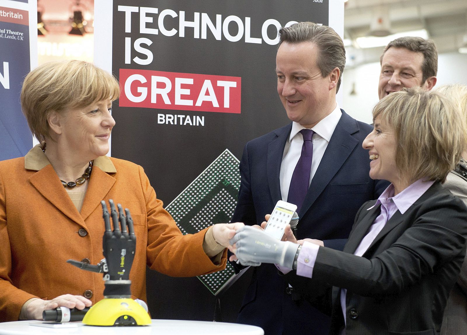Angela Merkel y David Cameron observan el funcionamiento de una mano biónica controlada desde un teléfono móvil.