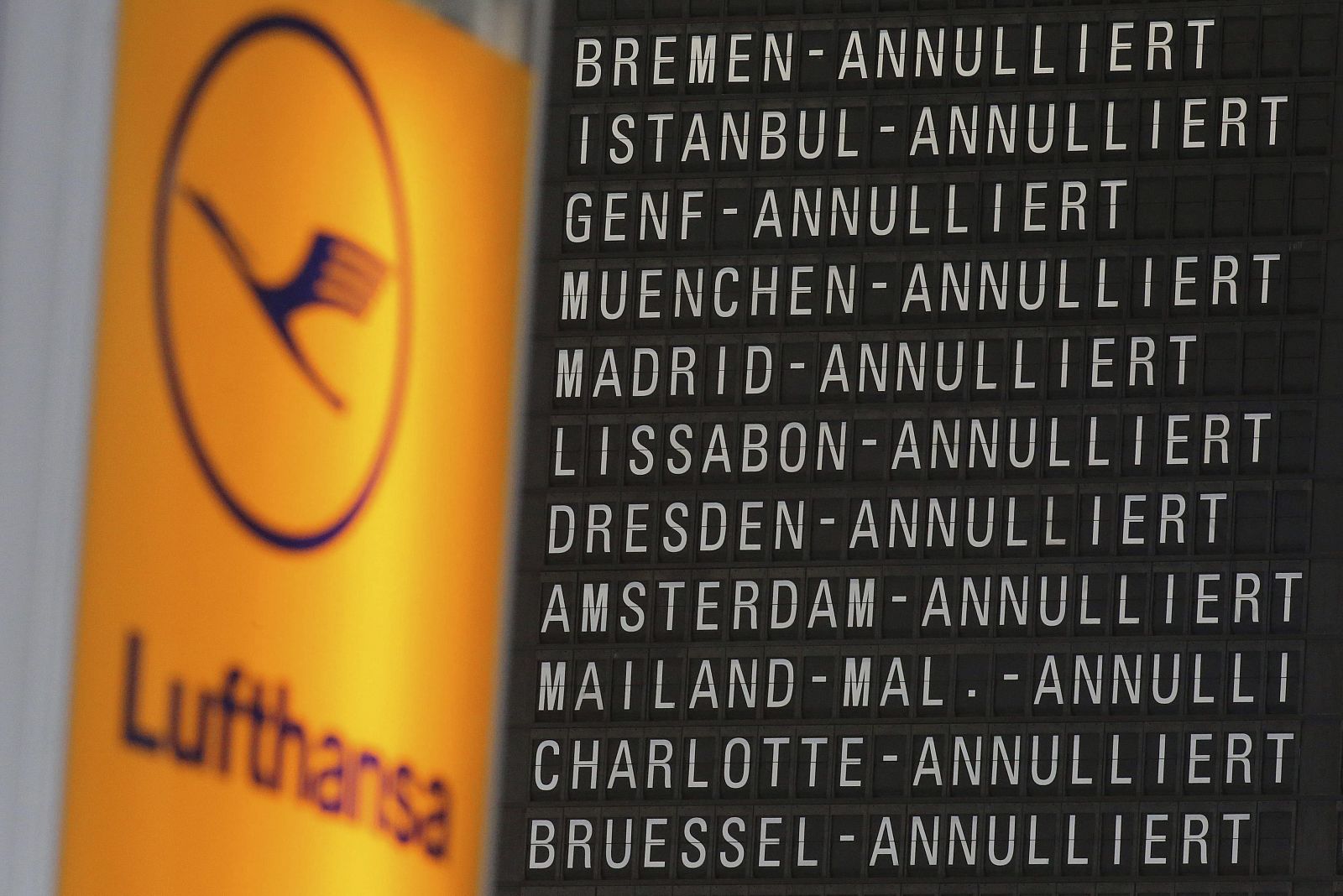 El logotipo de la aerolínea alemana Lufthansa permanece junto a una pantalla que muestra cómo la mayoría de los vuelos de la compañía han sido cancelados, en el aeropuerto de Fráncfort (Alemania)