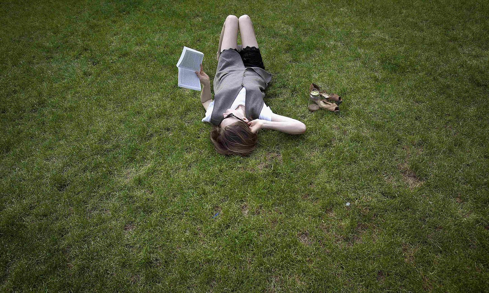 A woman lies in the grass while reading a book, at Columbia University in New York