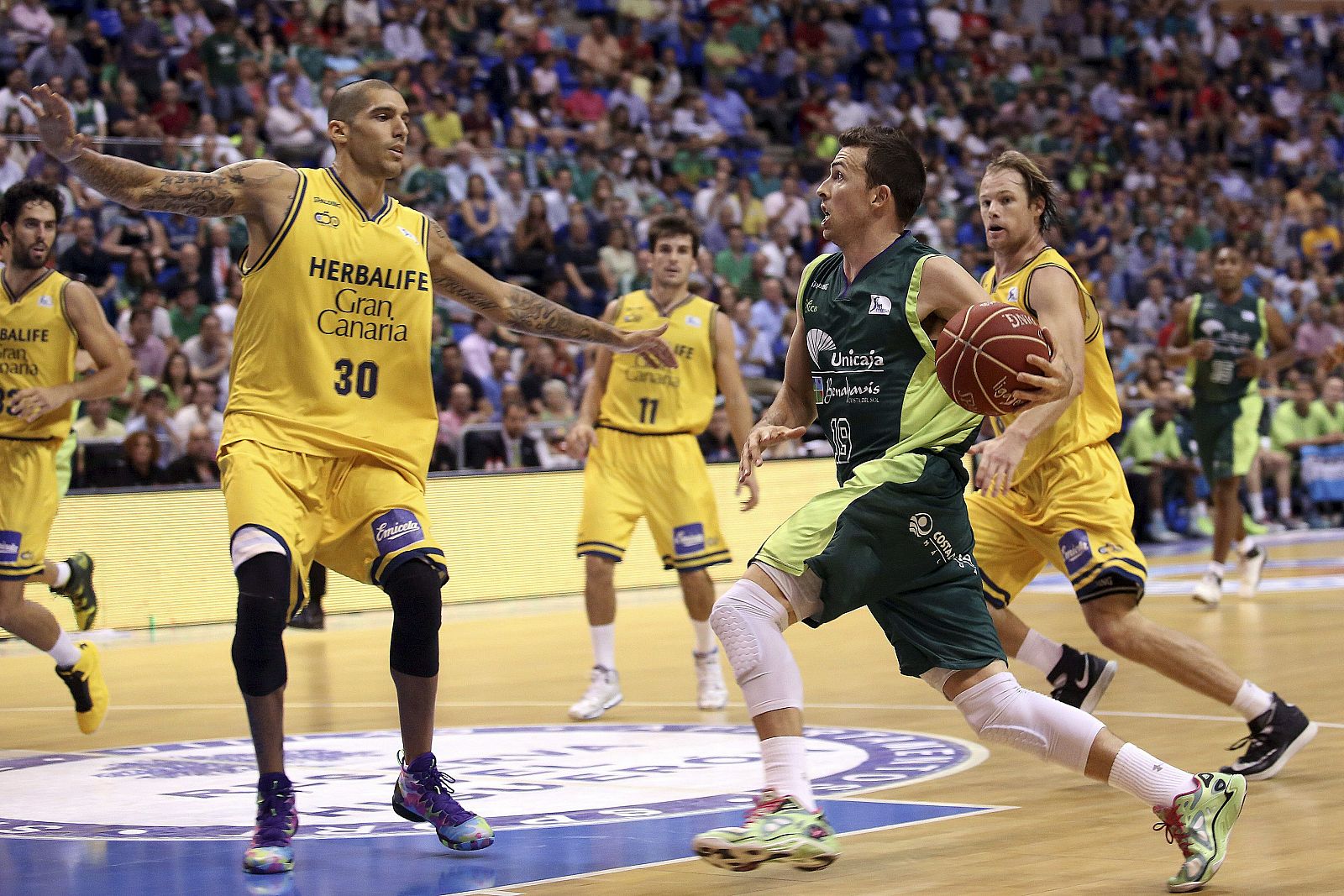 El escolta del Unicaja Ryan Toolson (c) entra a canasta ante la defensa del ala-pivot Nacho Martín (i), del Herbalife Gran Canaria