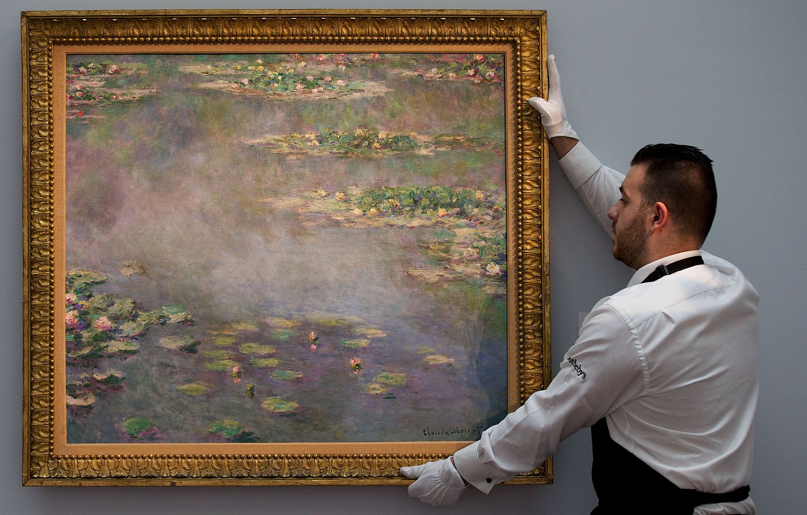 Un empleado de Sotheby's coloca un cuadro de la serie 'Los nenúfares' subastado en Londres por 29,7 millones de euros.