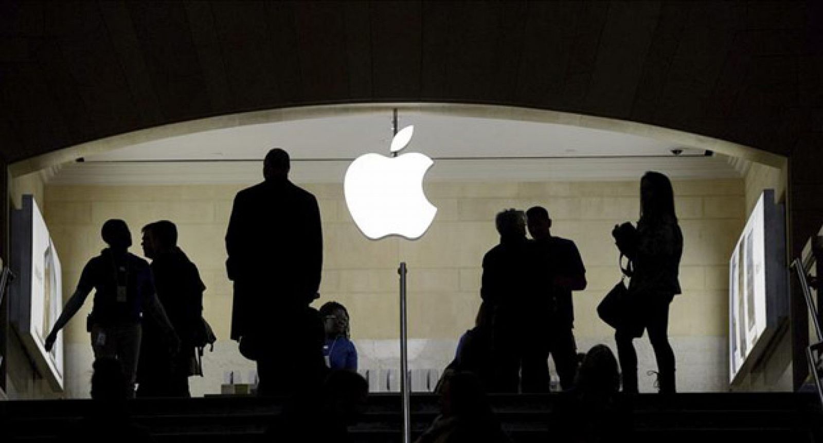 Viandantes pasan bajo un logo iluminado de Apple.