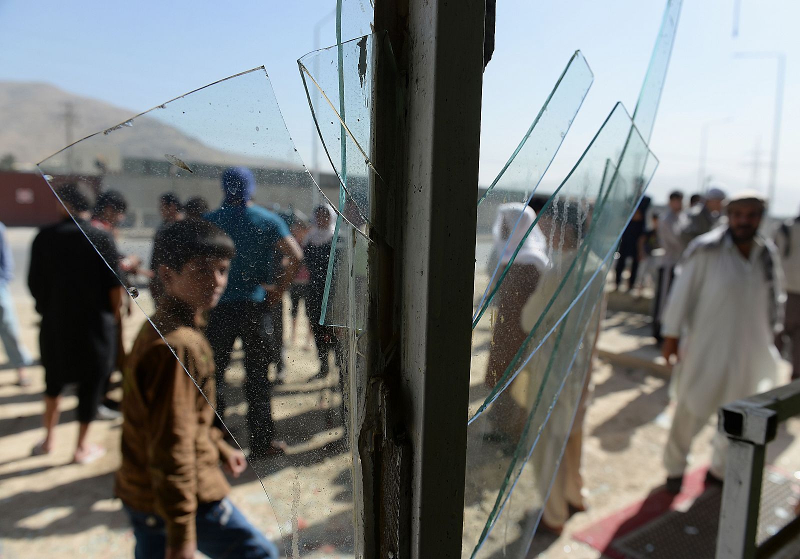 Los afganos se ven a través del cristal roto en una tienda en el lugar del ataque suicida en Kabul.