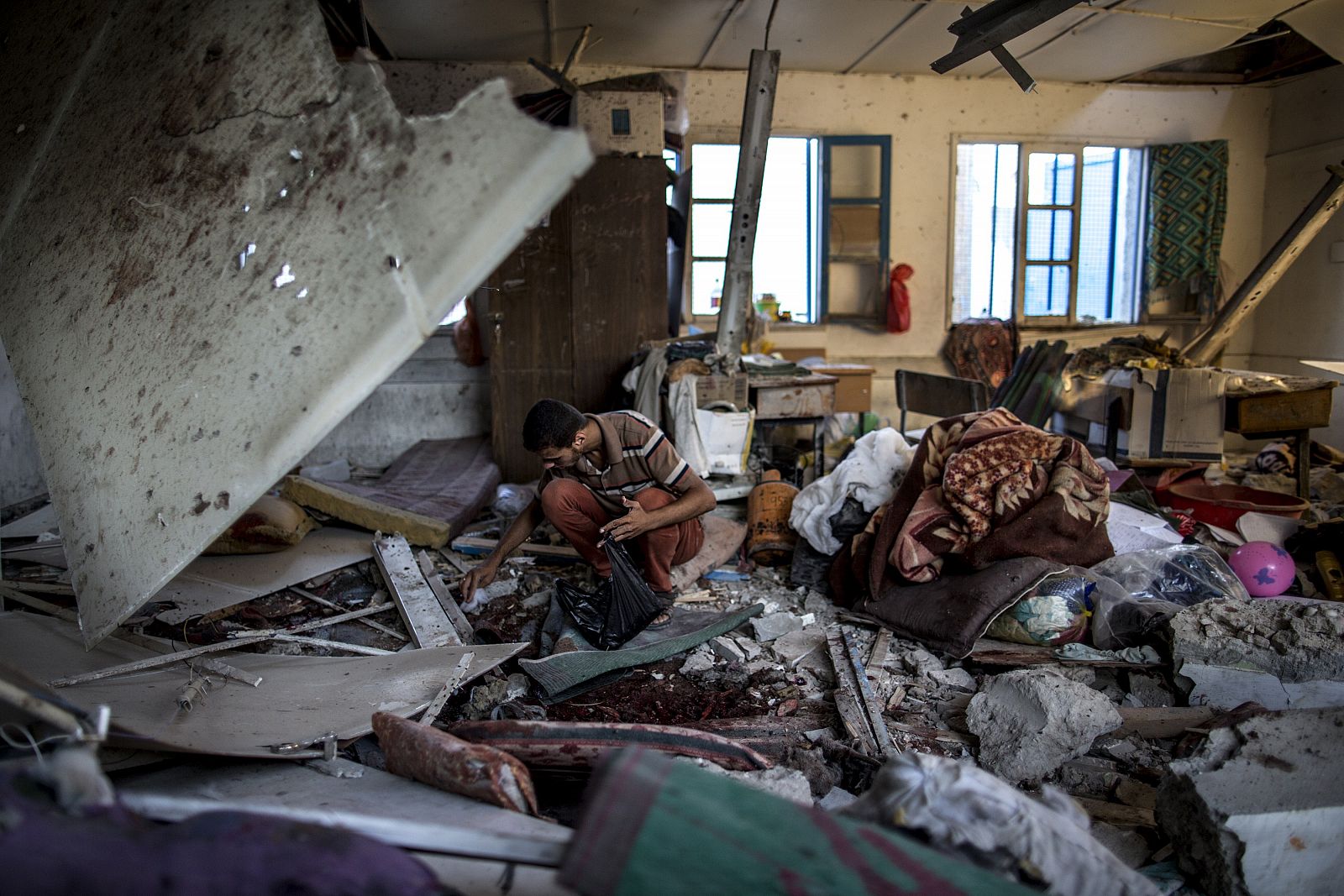 Un palestino recoge los restos de una sala de clases en el interior de la escuela de la ONU en Jabaliya