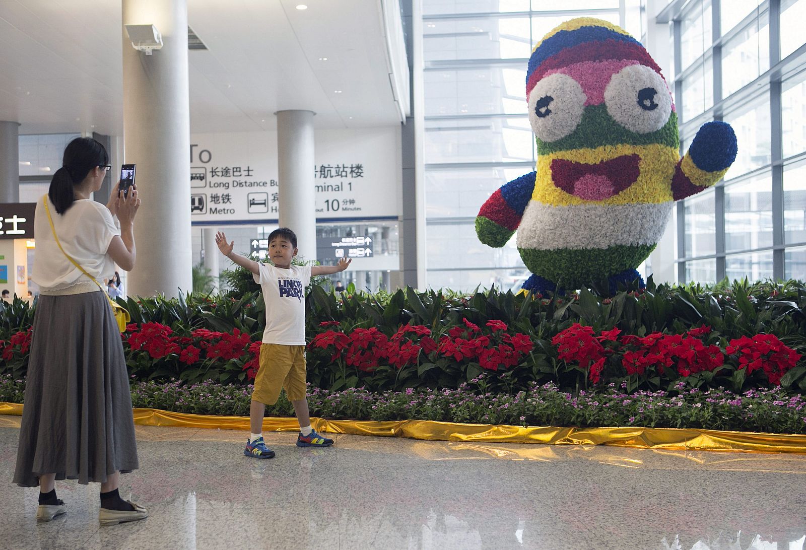 Una mujer saca una fotografía a un niño junto a 'Nankín Lele', la mascota oficial de los Juegos Olímpicos de la Juventud en el aeropuerto de Nankín (China).