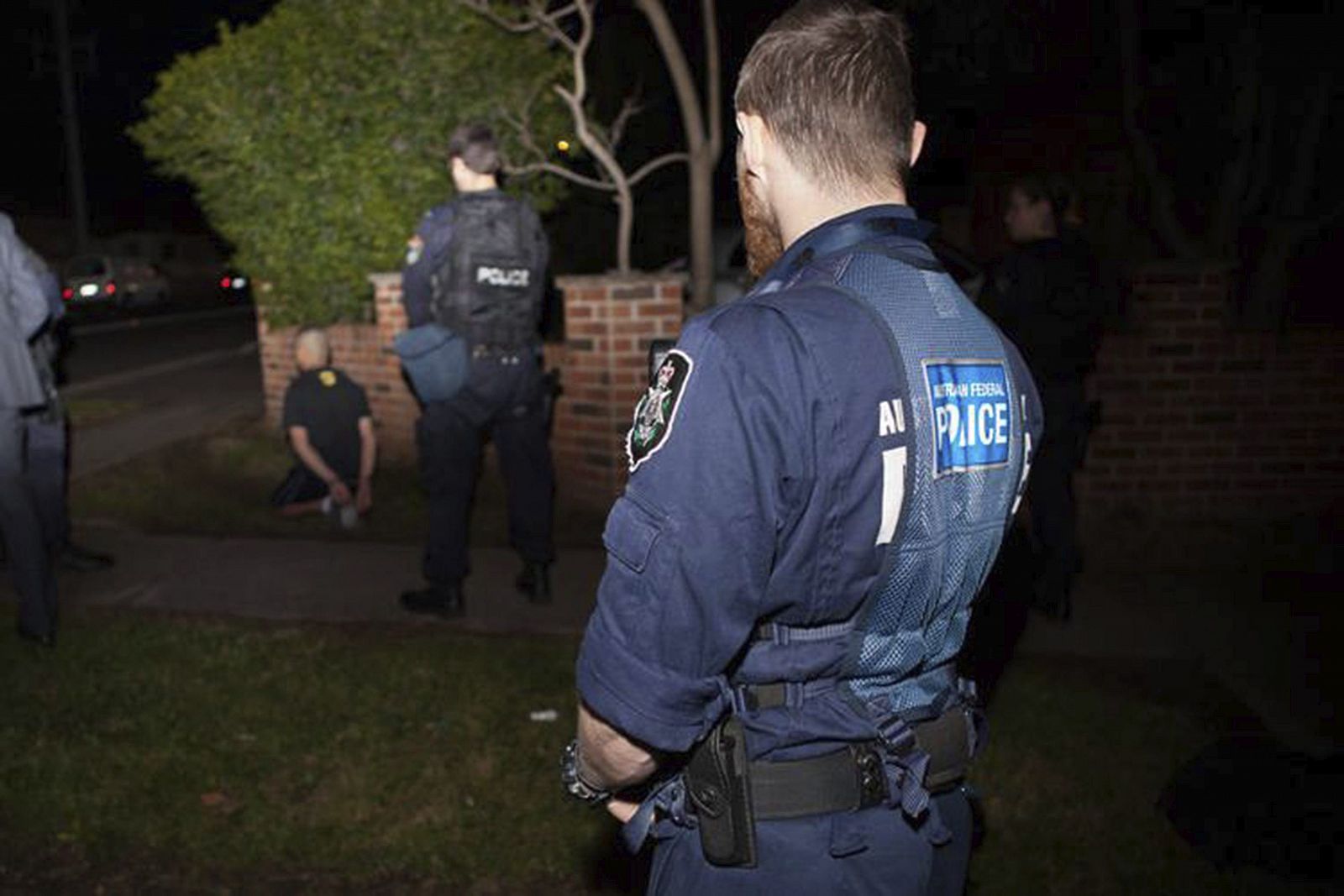 Fotografía facilitada por la Policía de Nueva Gales del Sur que muestra a policías que vigilan a un detenido en la macroperación terrorista a las afueras de Sidney.
