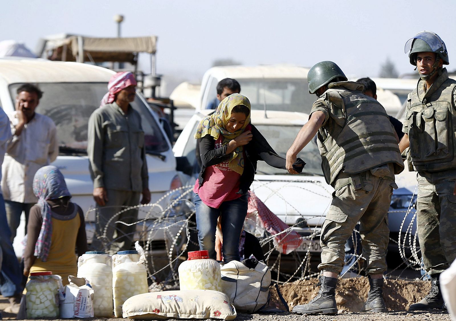 Un soldado turco ayuda a una mujer a cruzar la alambrada en la frontera entre Siria y Turquía