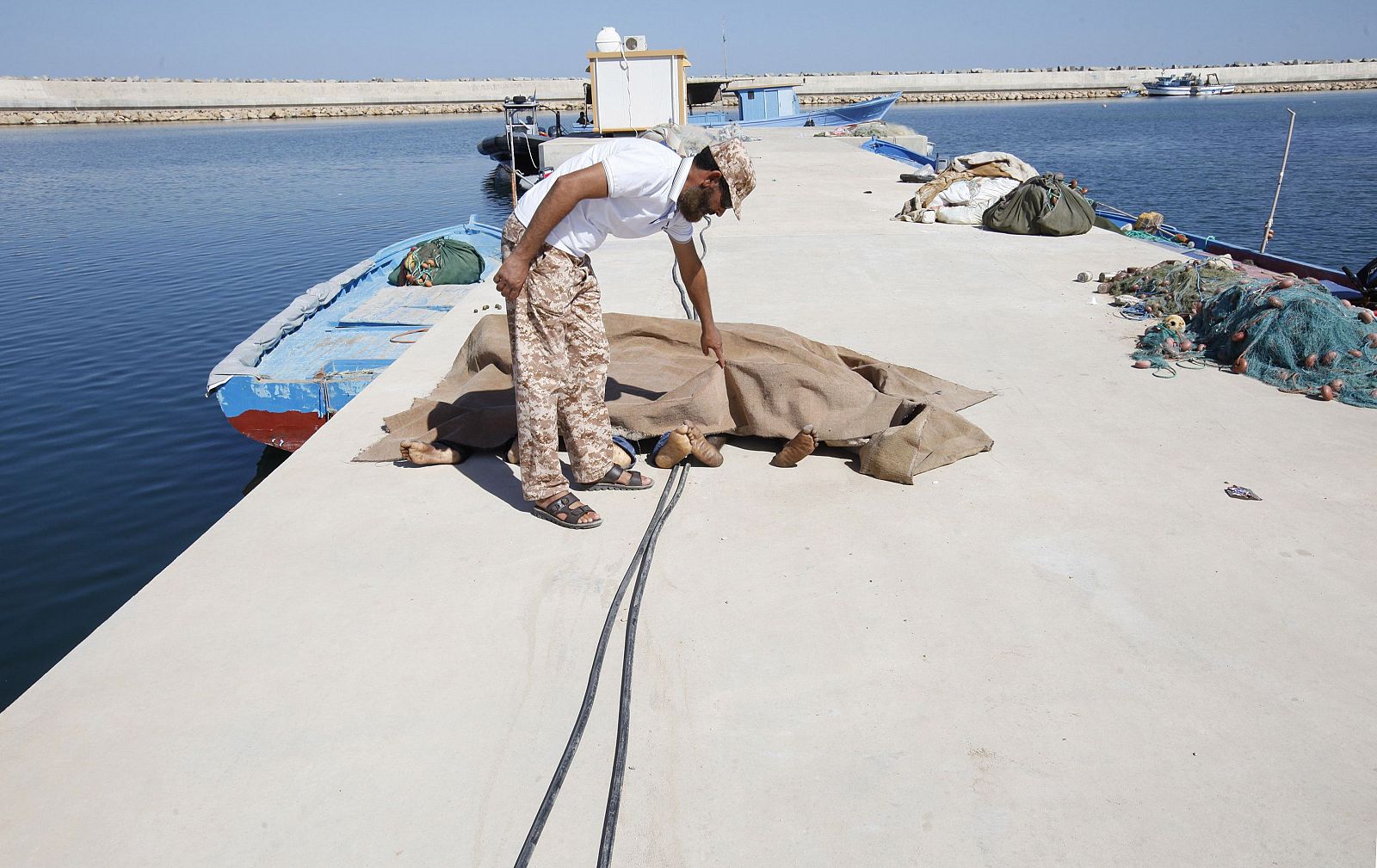 A man inspects the bodies of three African migrants that were recovered by the Libyan coastguard, after their boat sunk off the coastal town of Garaboly, al este de la capital Trípolo, a mediados de este mes.